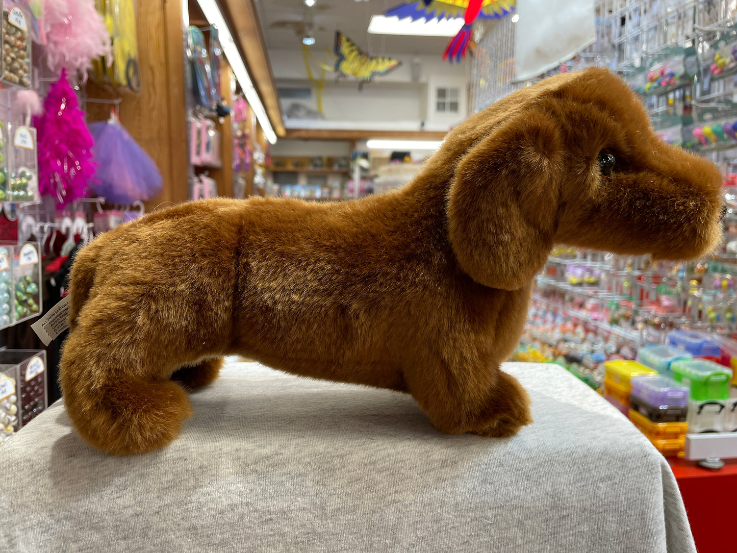 Red Dachshund plush toy on display in colorful toy store, showcasing long body and short legs characteristic of breed