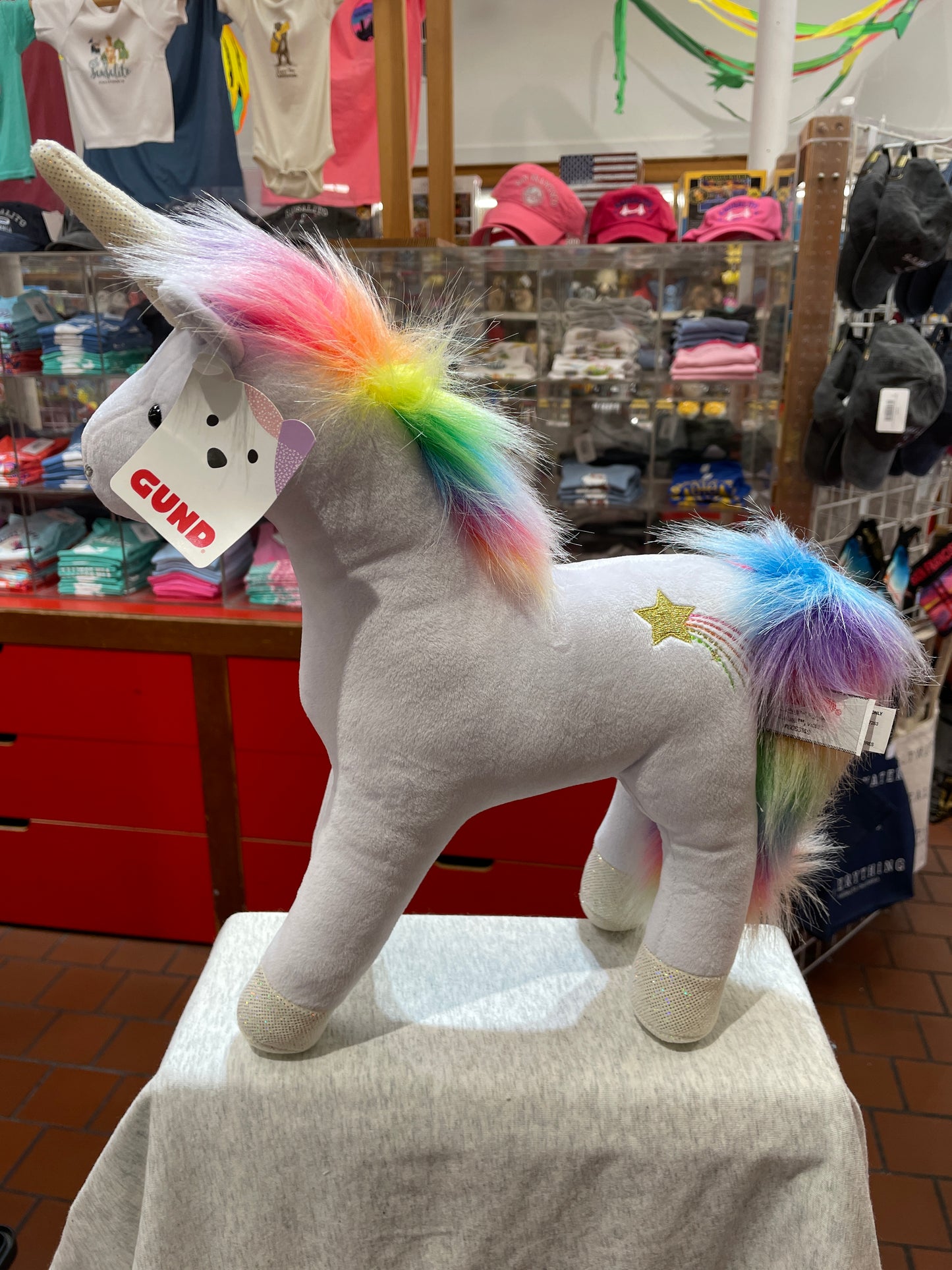 Gund Bluebell unicorn plush toy with rainbow mane and tail, sparkly horn, and embroidered star displayed in store