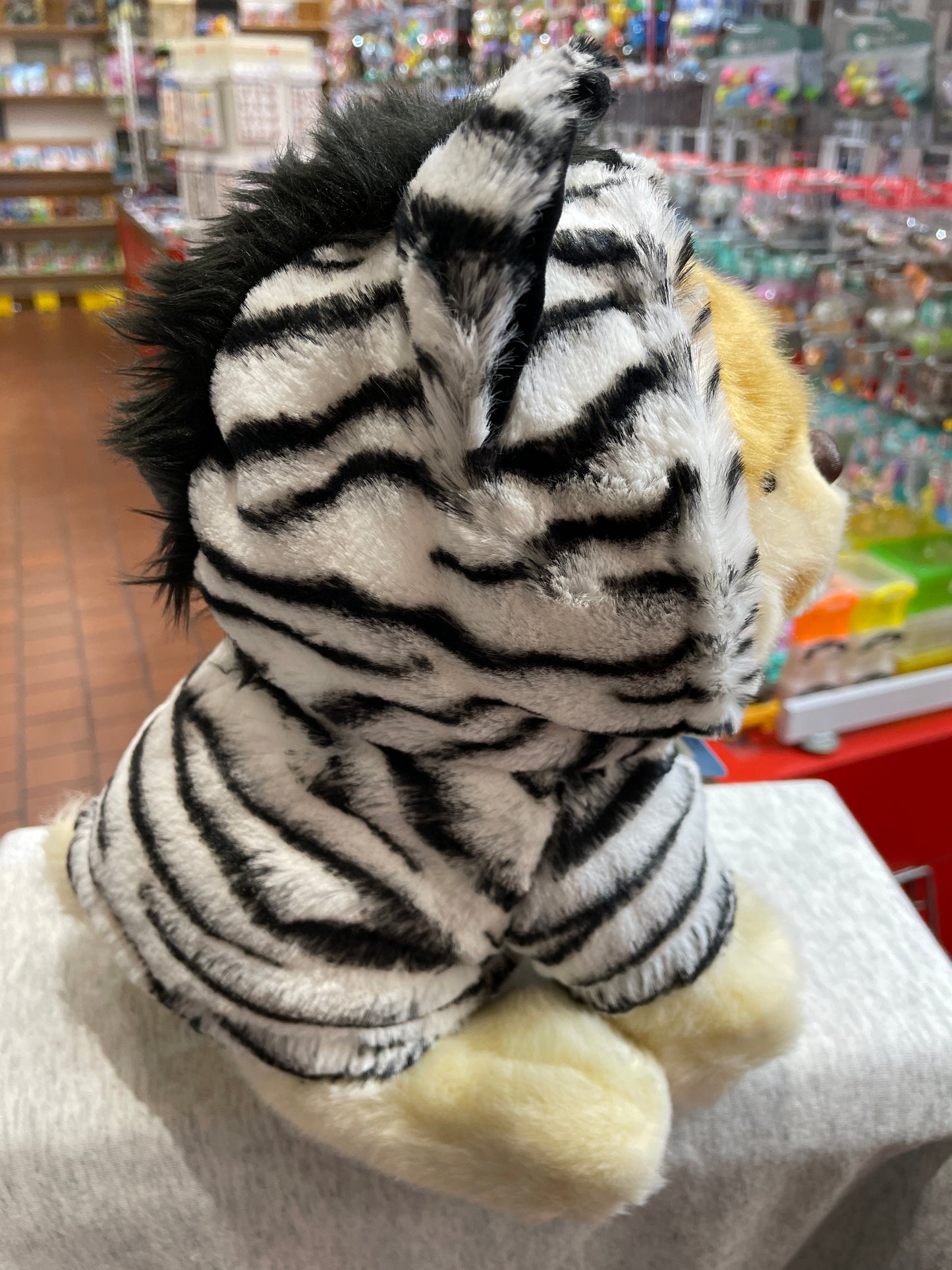 Gund World's Cutest Dog Boo plush toy in zebra outfit with fluffy mane, displayed in toy store
