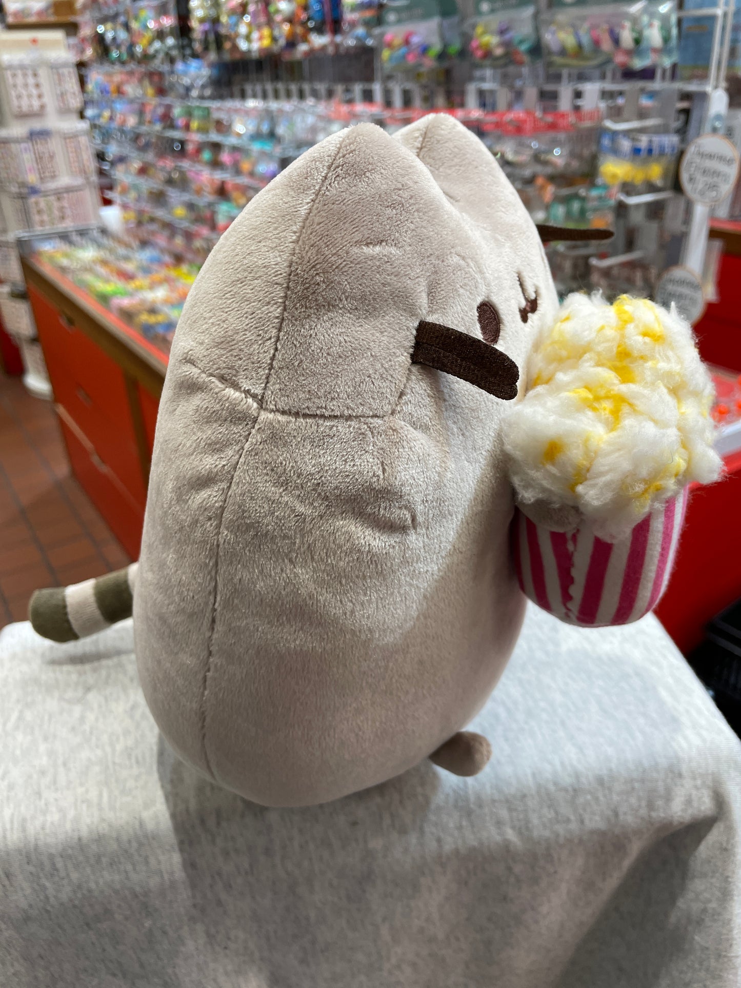 Gund Pusheen plush cat holding popcorn bucket, displayed in toy store aisle