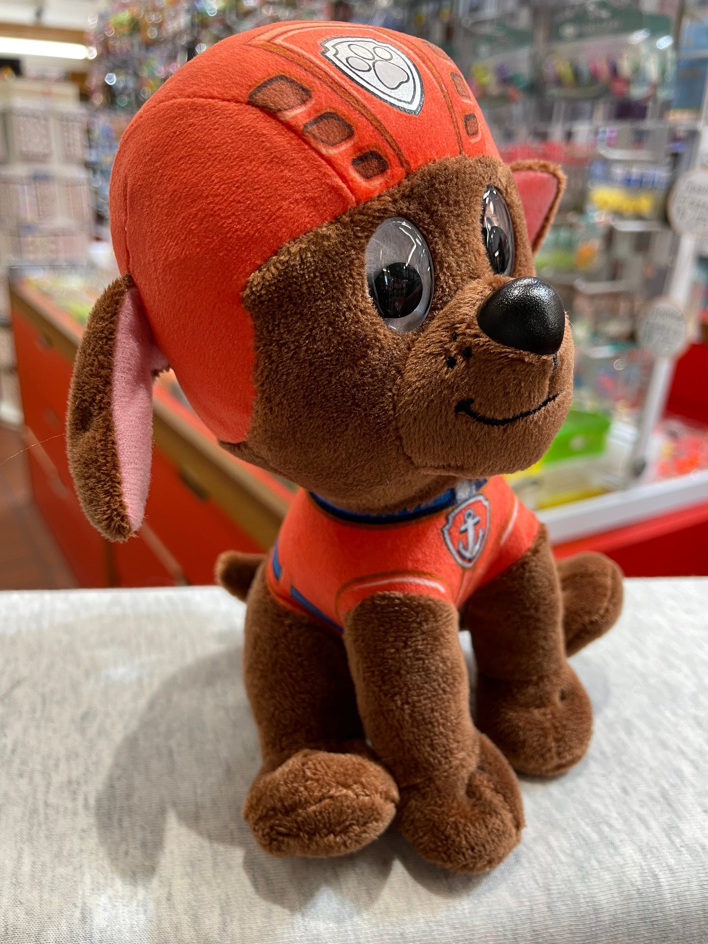 Gund Paw Patrol Zuma plush toy, brown puppy in orange diving uniform and helmet, smiling with shiny eyes, on store shelf