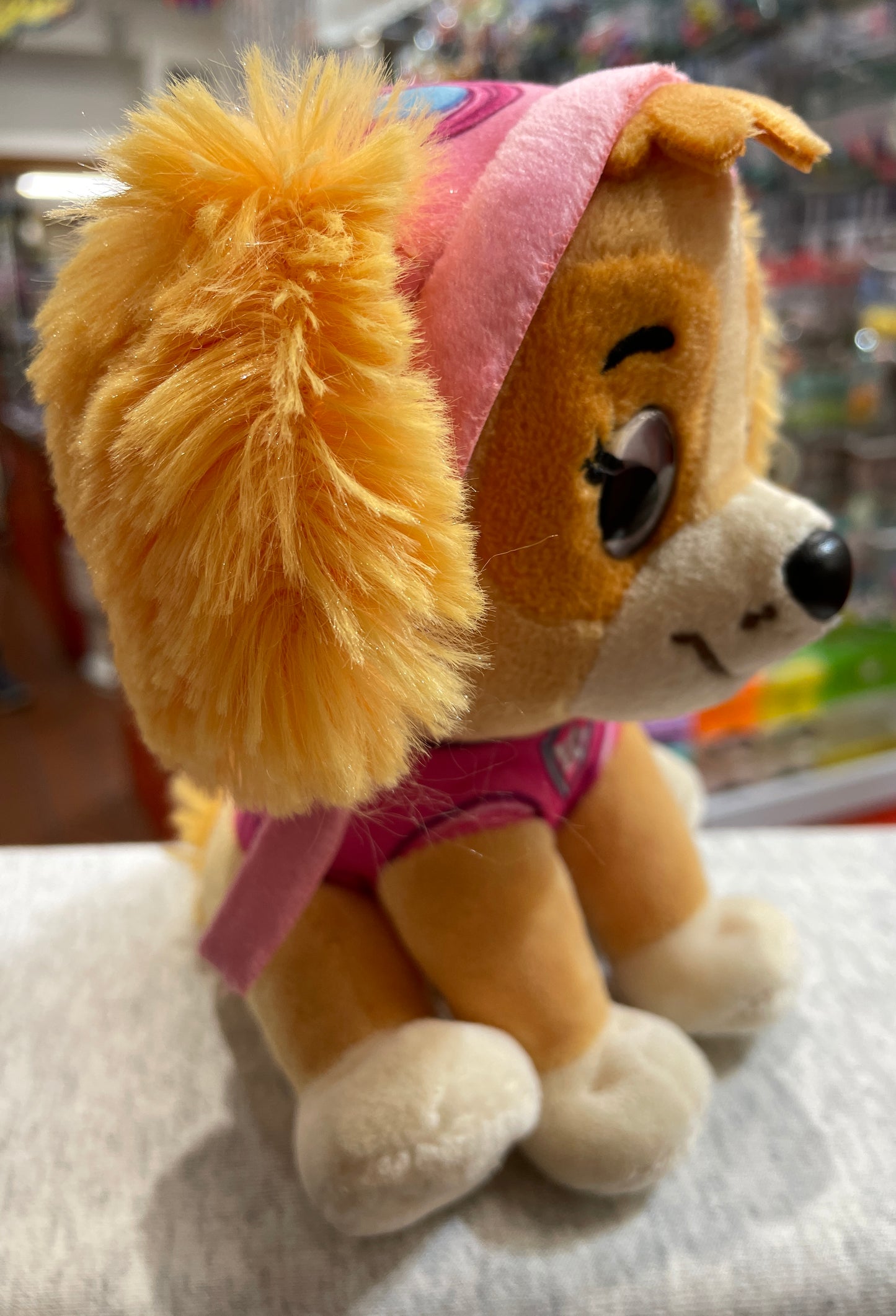 Gund Paw Patrol Skye plush toy, featuring yellow fur, pink pilot uniform, and smiling face, sitting on display shelf