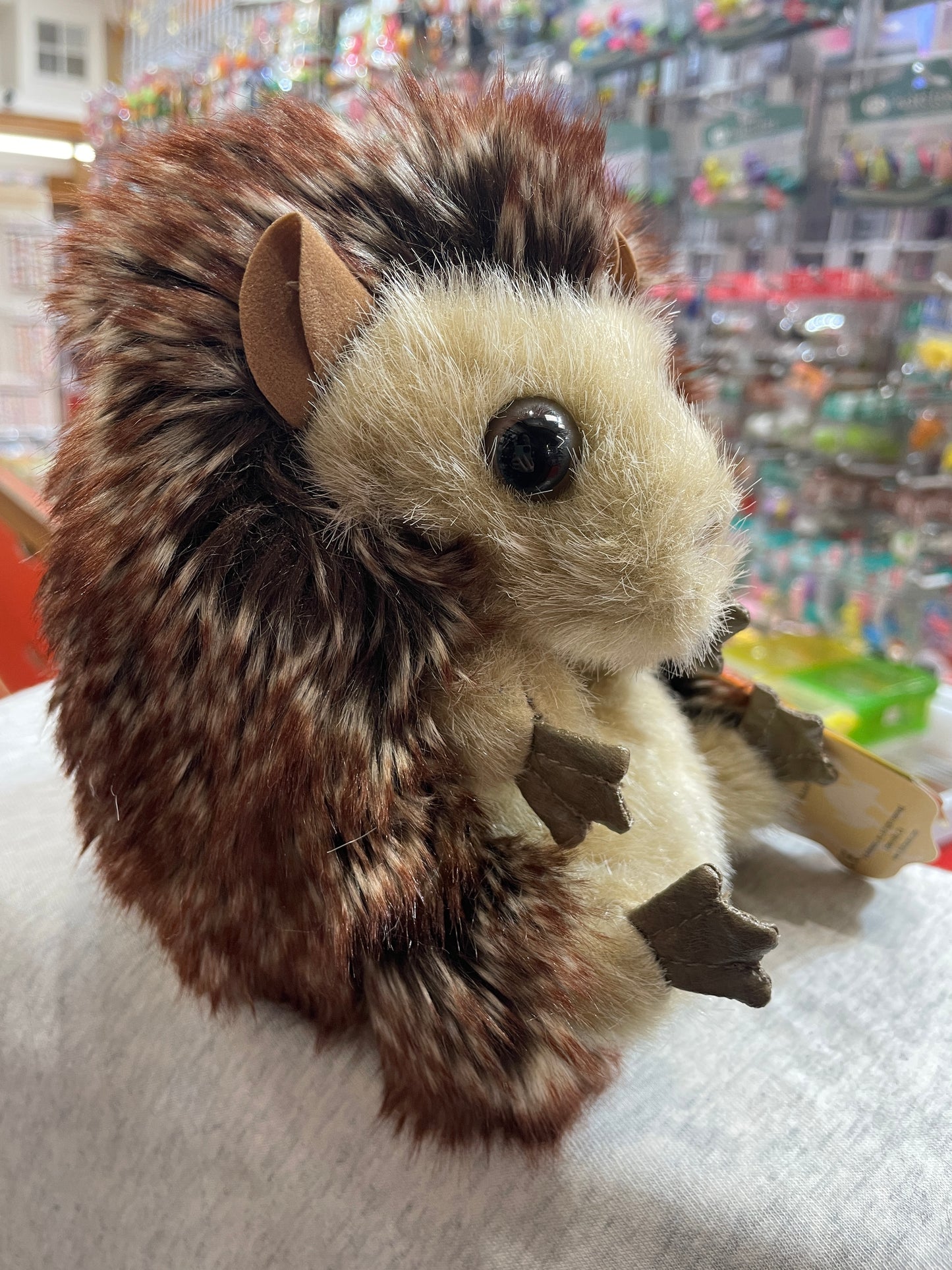 Folkmanis Hedgehog hand puppet with soft plush face, shaggier back, and five finger slots, displayed in a toy store setting