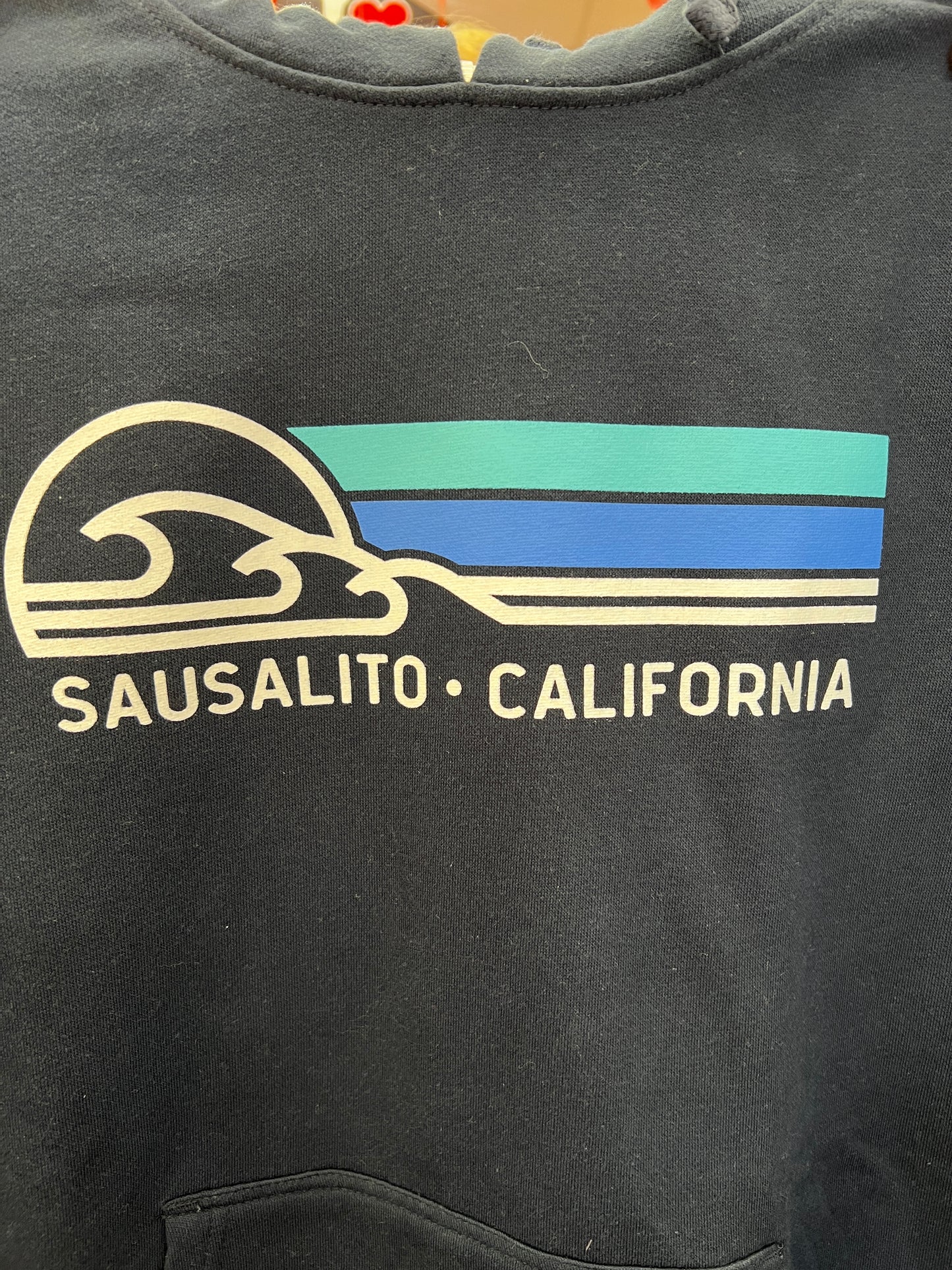 Sausalito California hoodie design with wave icon and blue bands on navy fabric, showcasing coastal-inspired graphic print