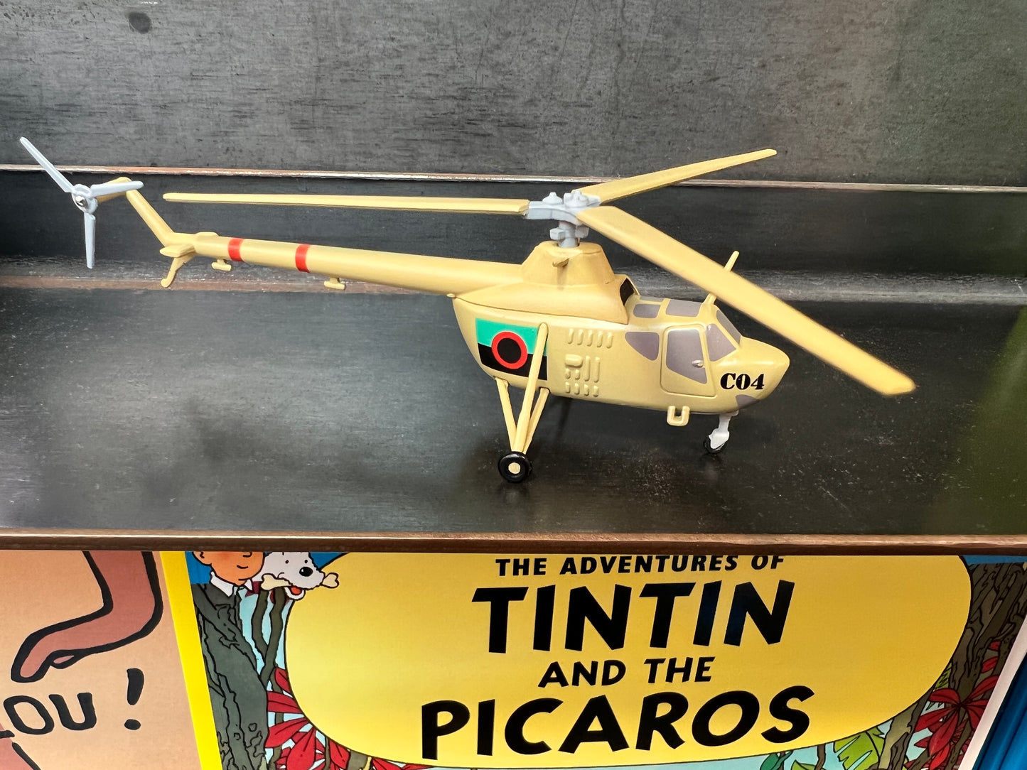 Model Mi-1 Hare helicopter from Tintin and the Picaros, beige with red stripes, displayed above comic book cover