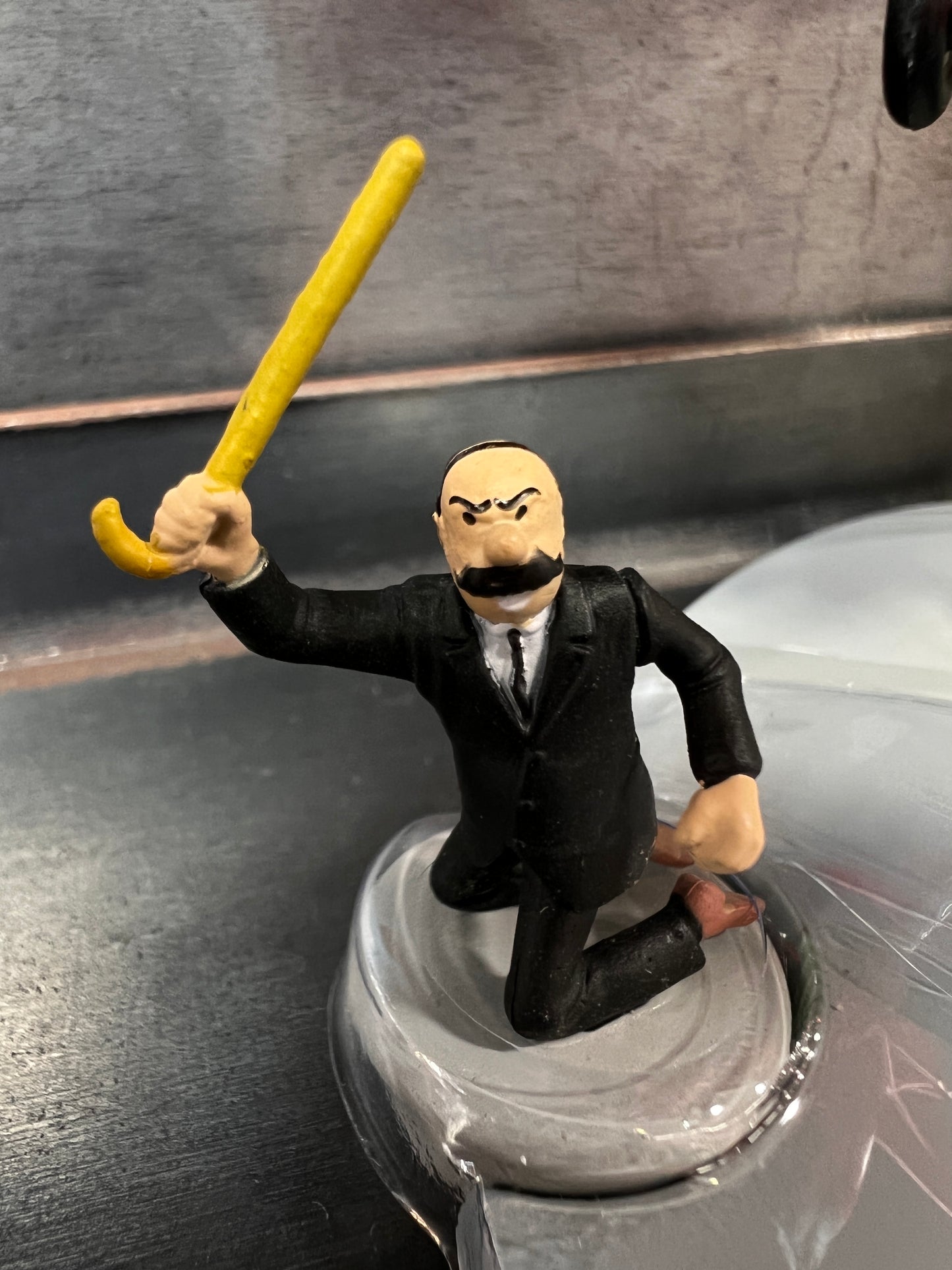 Tintin character figurine waving yellow cane, from "The Black Island" adventure, with Dewoitine D-27 plane in background