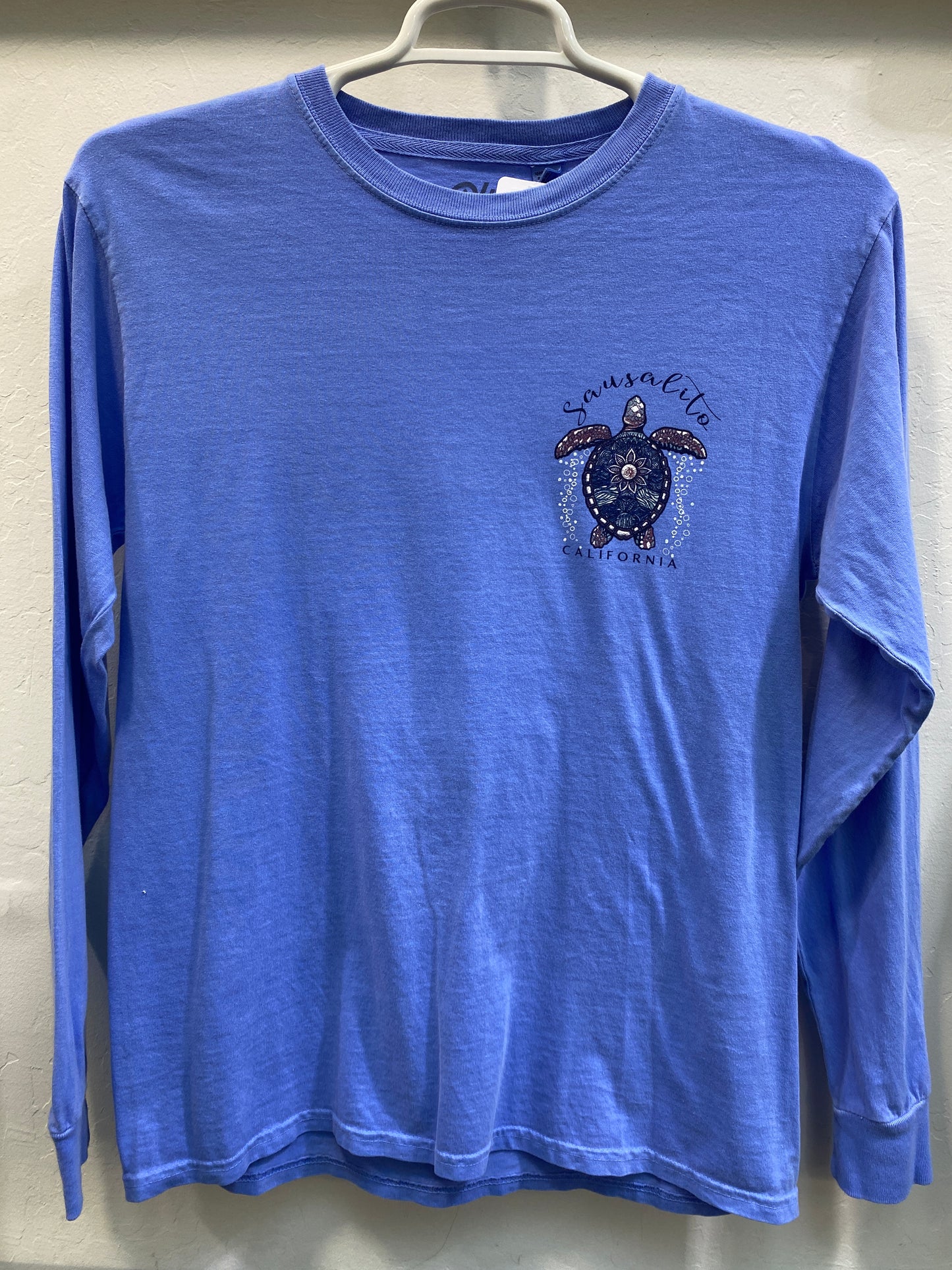 Blue long sleeve t-shirt with Sausalito turtle mandala design, hanging on display for souvenir merchandise