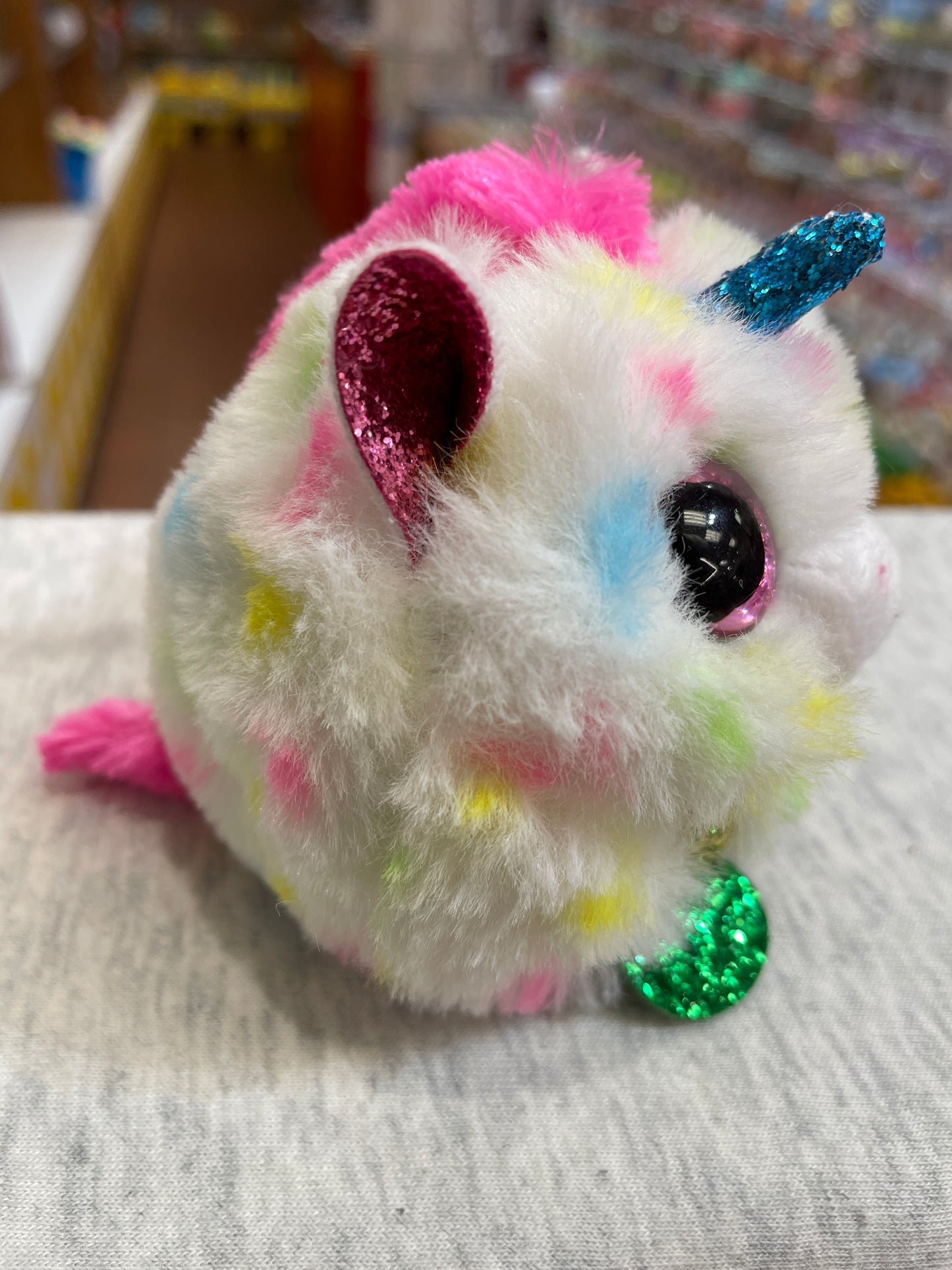 Colorful Ty Puffies Harmonie speckled unicorn plush toy with glittery horn, ears, and feet, sitting on fabric surface