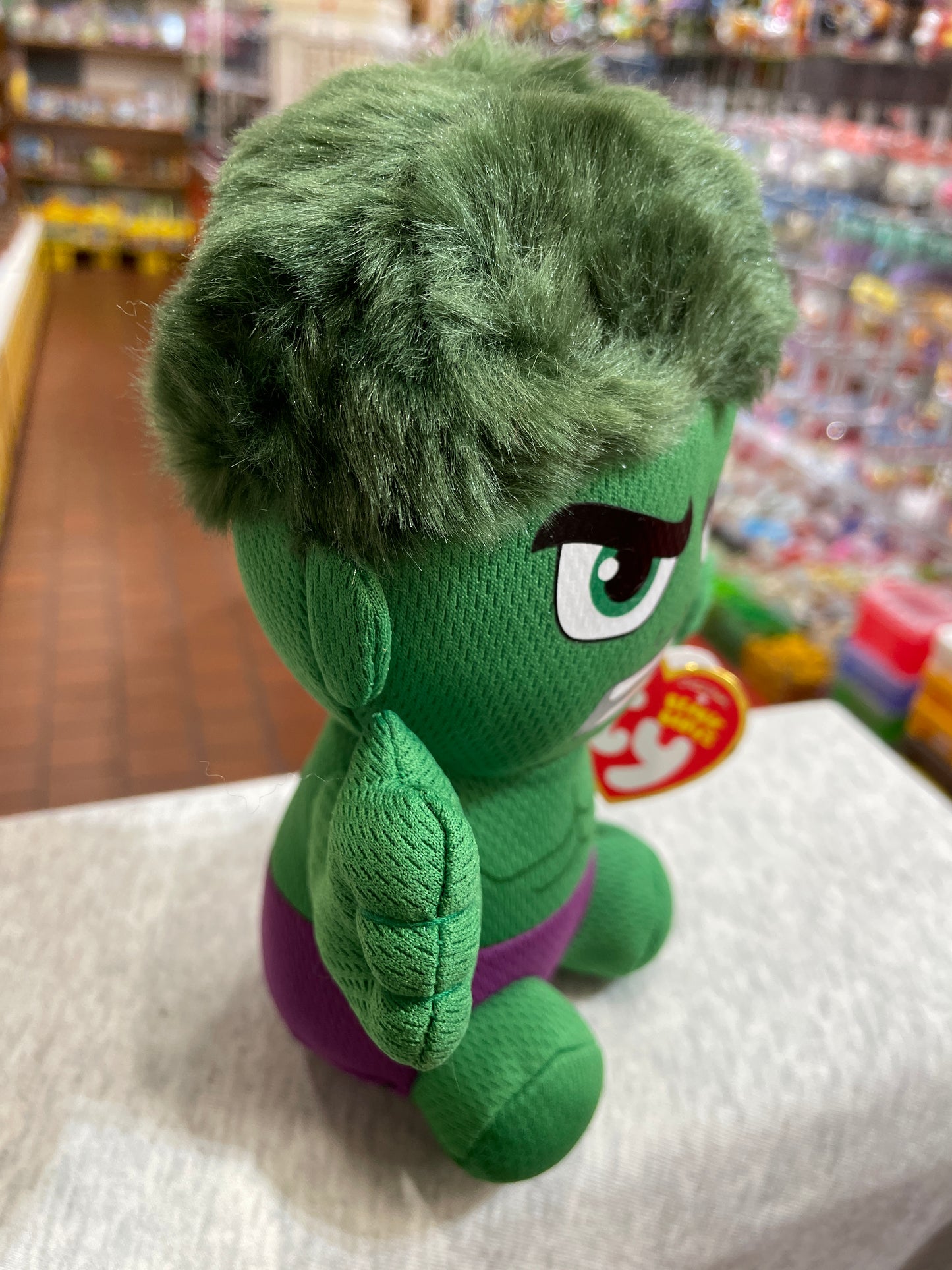Ty Beanie Baby Hulk plush toy with green fur, purple shorts, and large eye, displayed in toy store aisle
