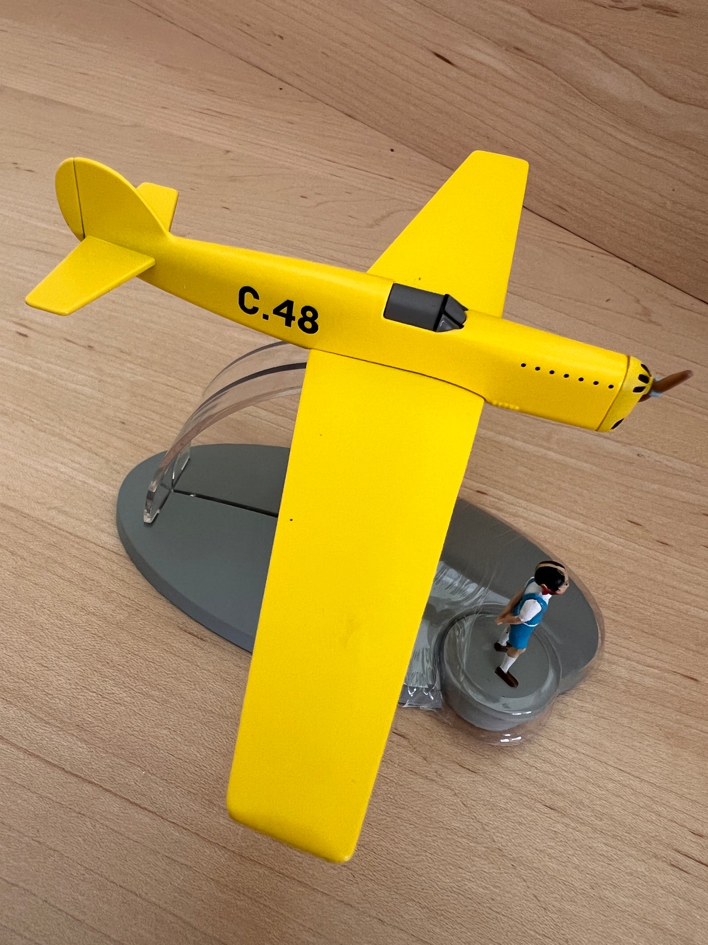 Prototype C.48 model plane from Jo, Zette and Jocko comic, bright yellow on stand with small figure below, wooden background