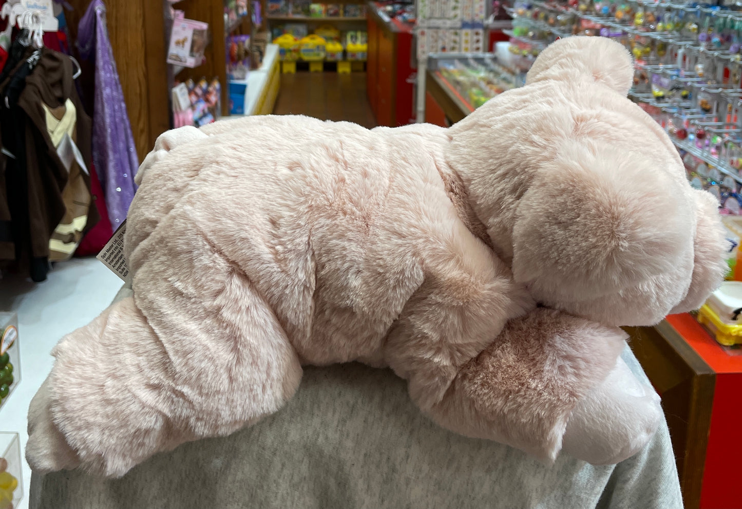 Soft blush pink Gund Hamlet pig plush toy displayed in toy store, showcasing plump body and curly tail