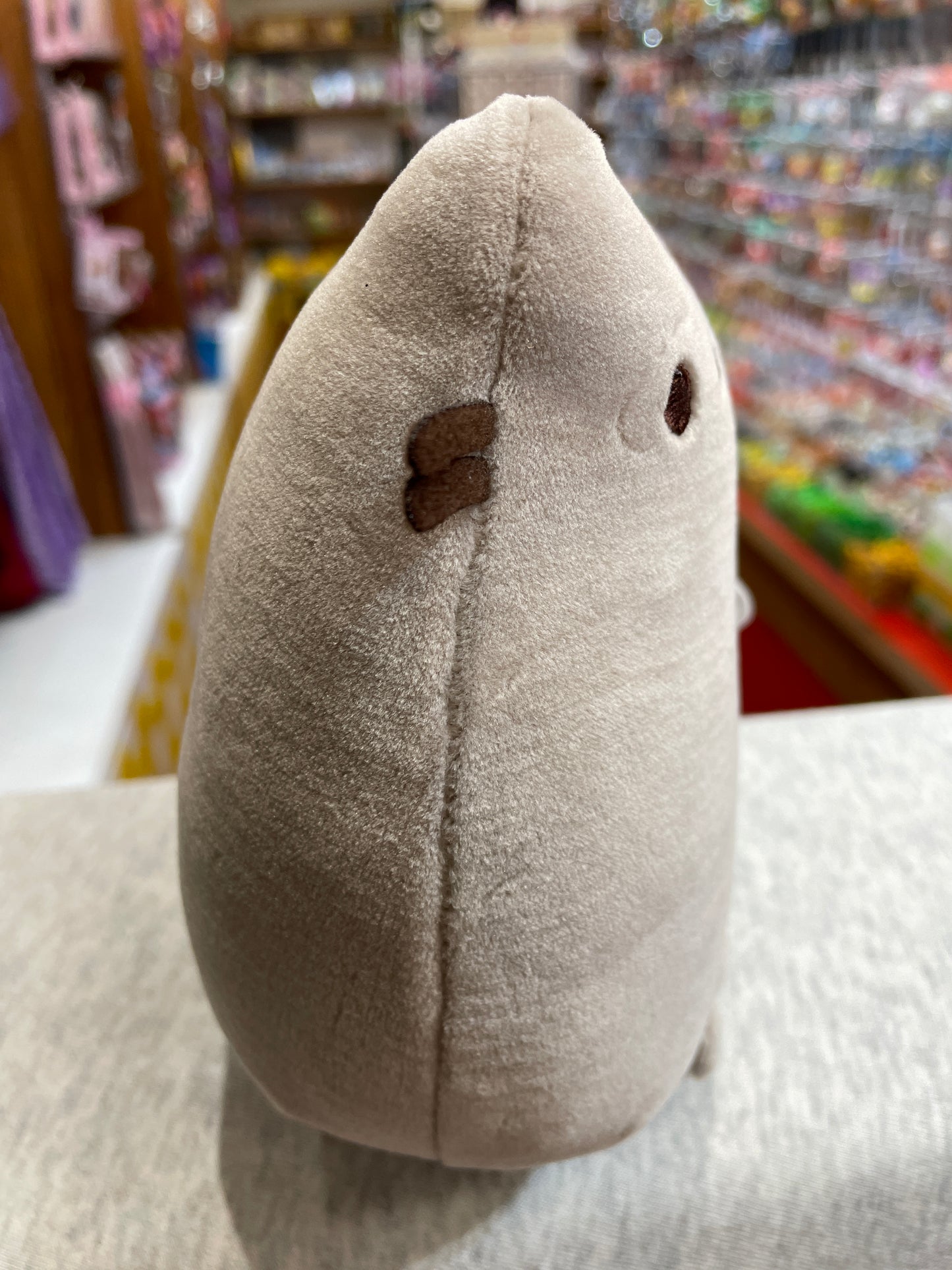 Soft gray Pusheen Squisheen plush toy in sitting pose, showcasing its squishy texture and signature cat features in a store setting
