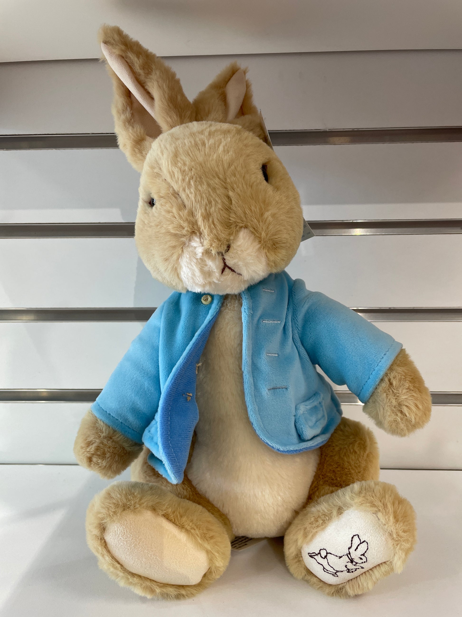 Gund Peter Rabbit plush toy in signature blue coat, with embroidered foot detail, sitting on display shelf