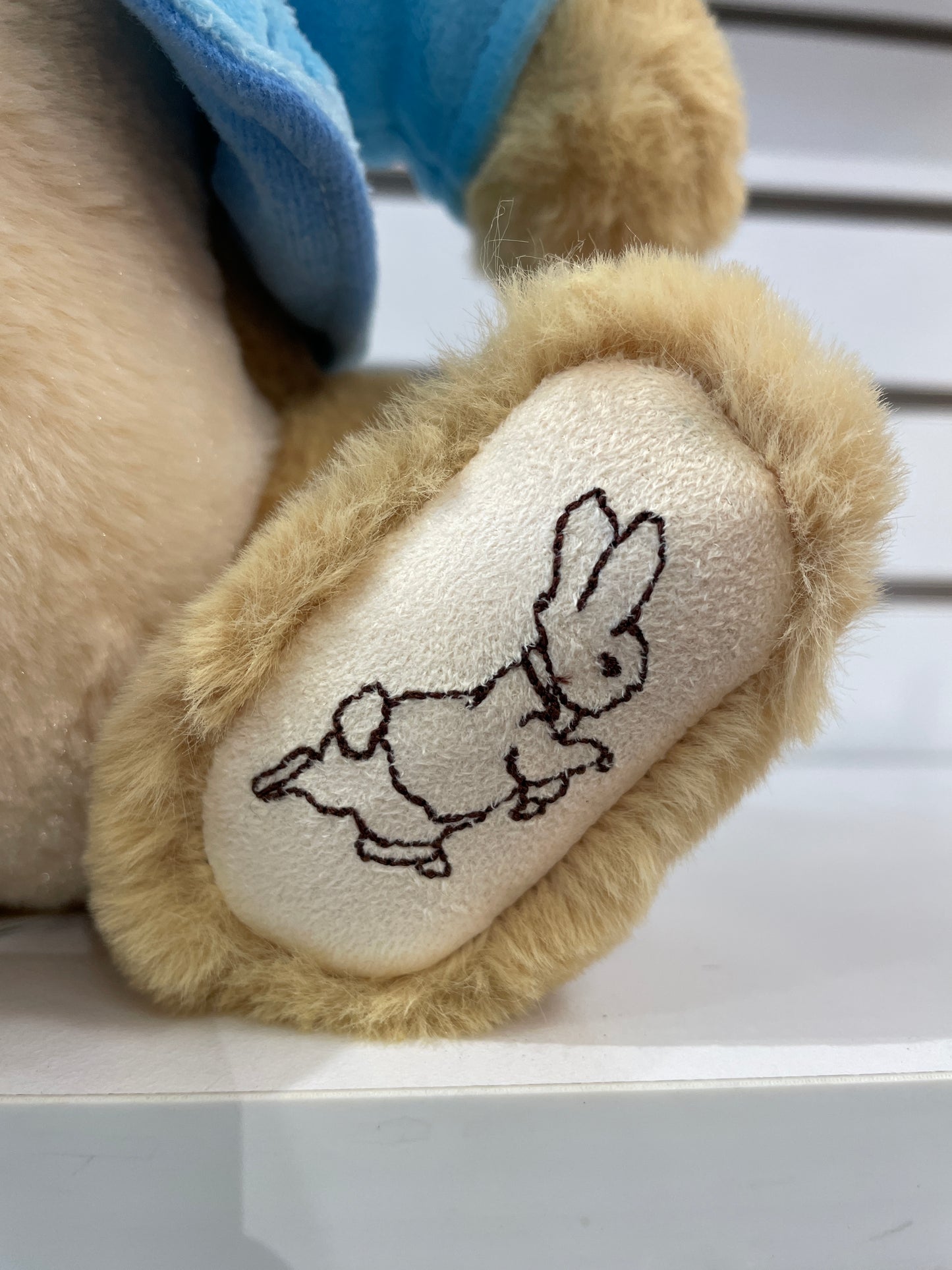 Gund Peter Rabbit plush foot with embroidered illustration of running rabbit, blue coat visible, on white surface
