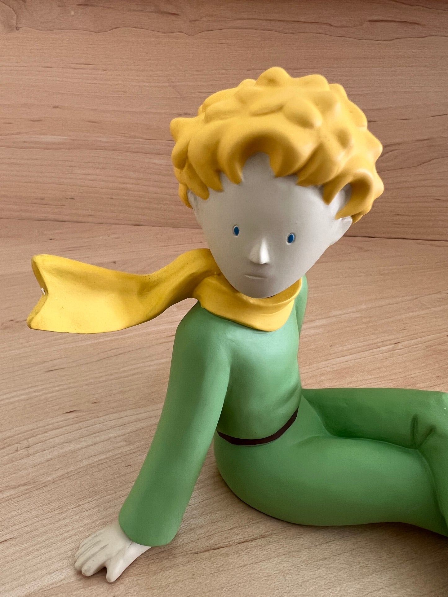 Le Petit Prince resin figure in green outfit with yellow scarf and hair, sitting on wooden surface, from 1997 collectible set