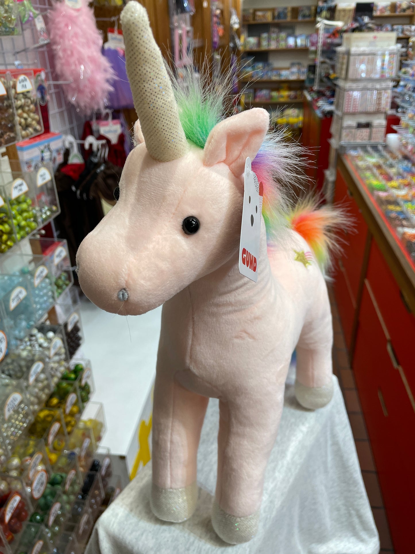 Gund Starflower Unicorn plush toy with pink body, sparkly horn, and rainbow mane standing in toy store display