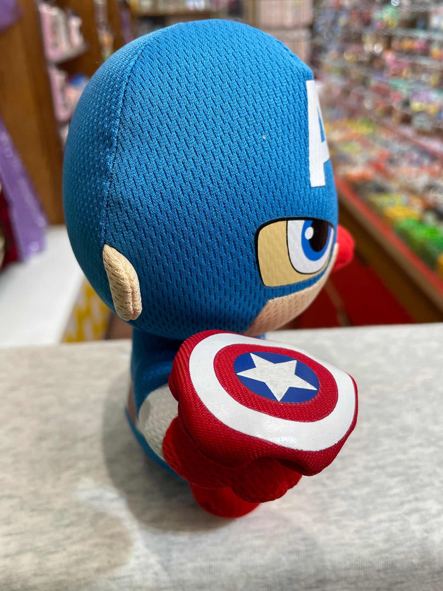 Ty Beanie Baby Captain America plush toy, blue mask with 'A', holding iconic shield, in toy store display