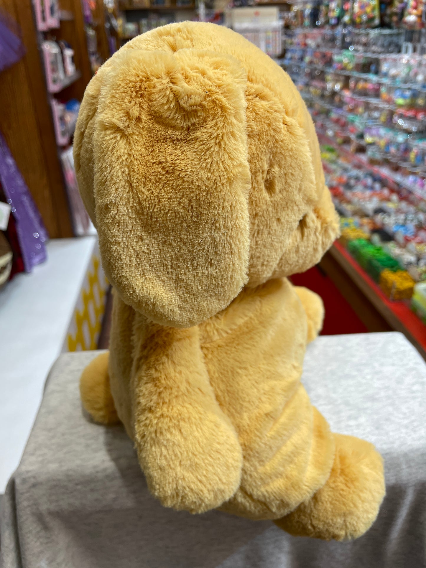 Soft peach-colored Baby Gund puppy plush toy with floppy ears, sitting on display in toy store