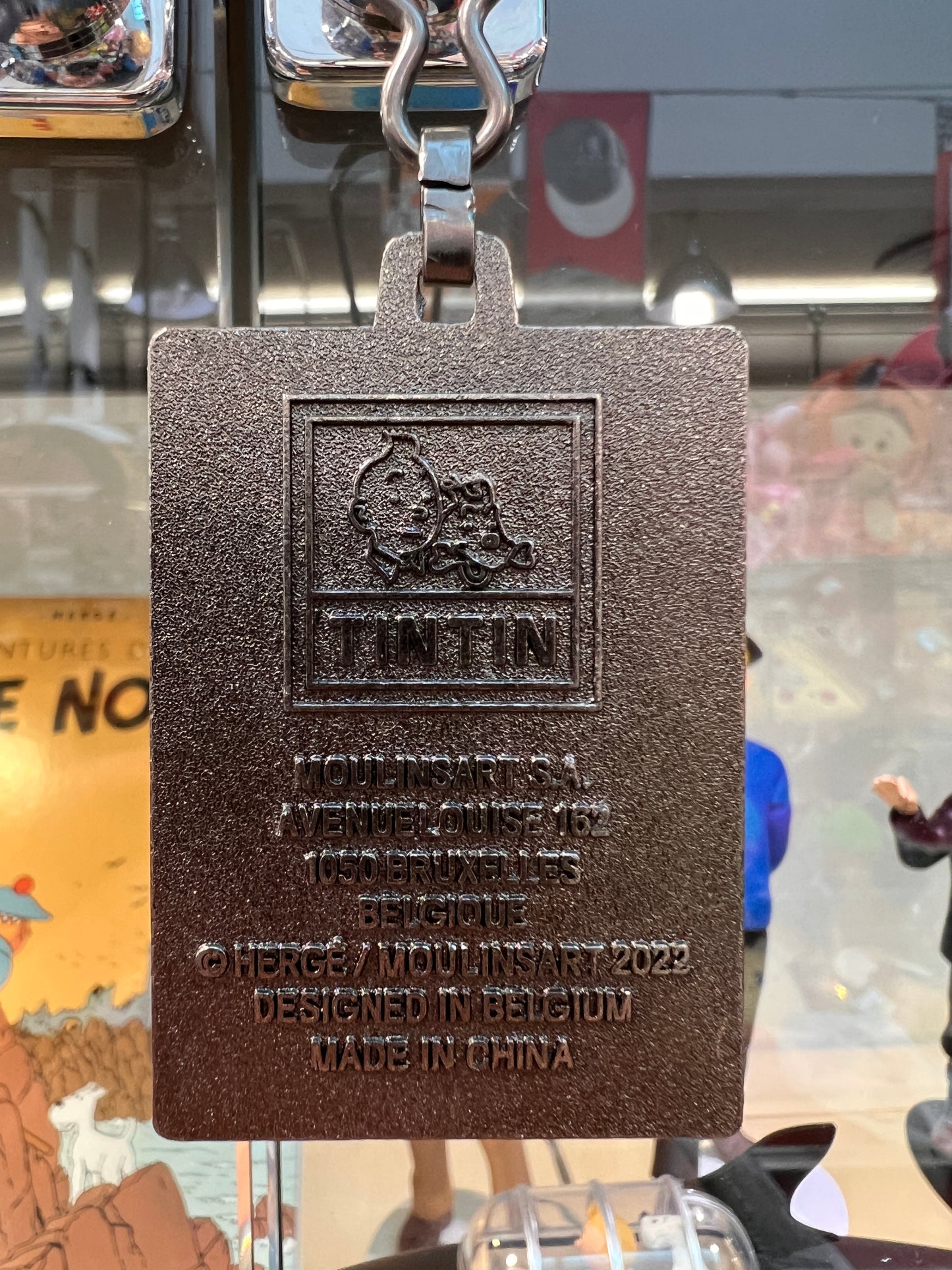 Metal Tintin keychain featuring embossed logo and text, displaying copyright information and "Designed in Belgium, Made in China"