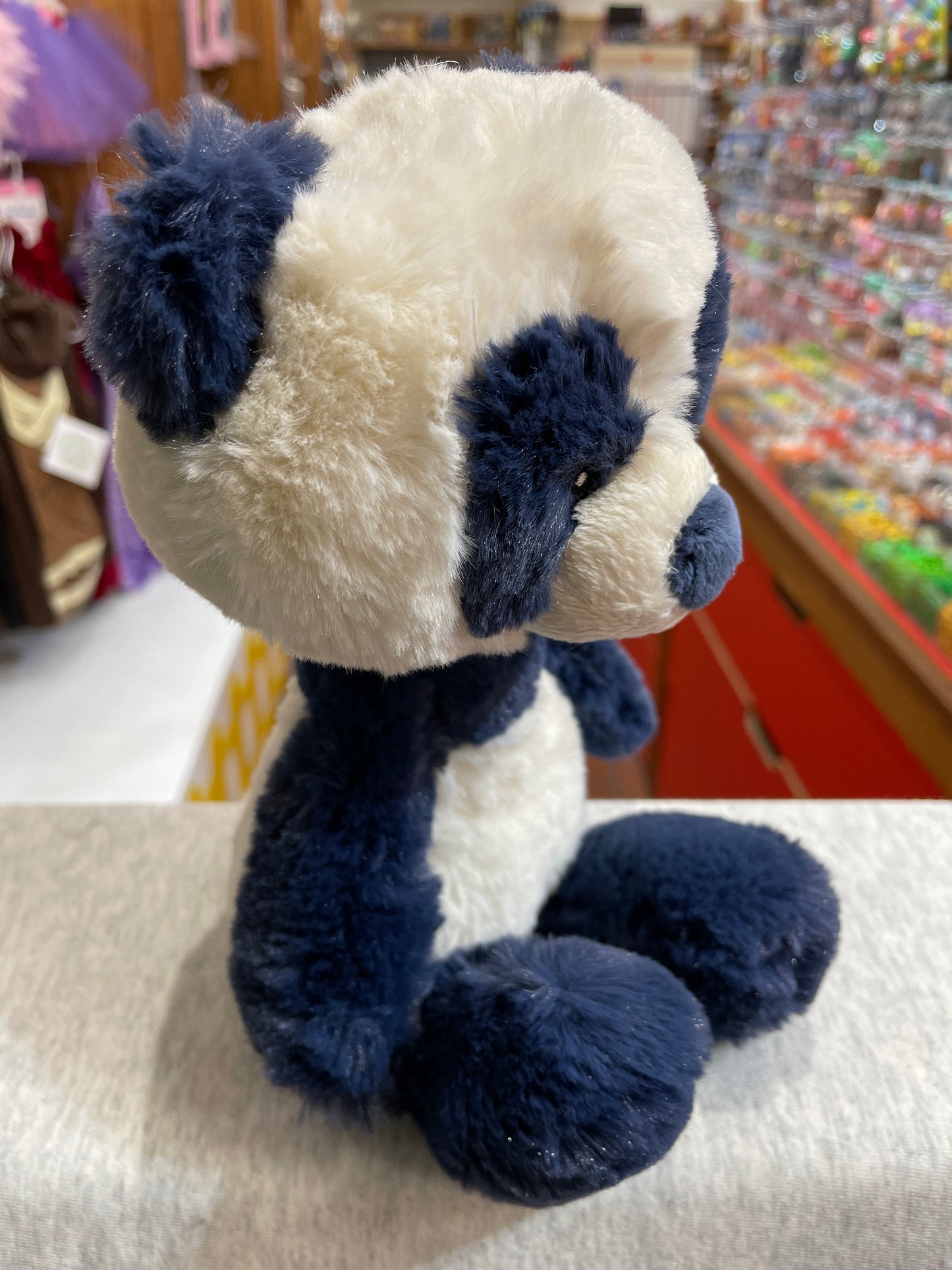 Soft plush Baby Gund panda toy in navy blue and cream, sitting on display in a toy store, perfect for nursery decor