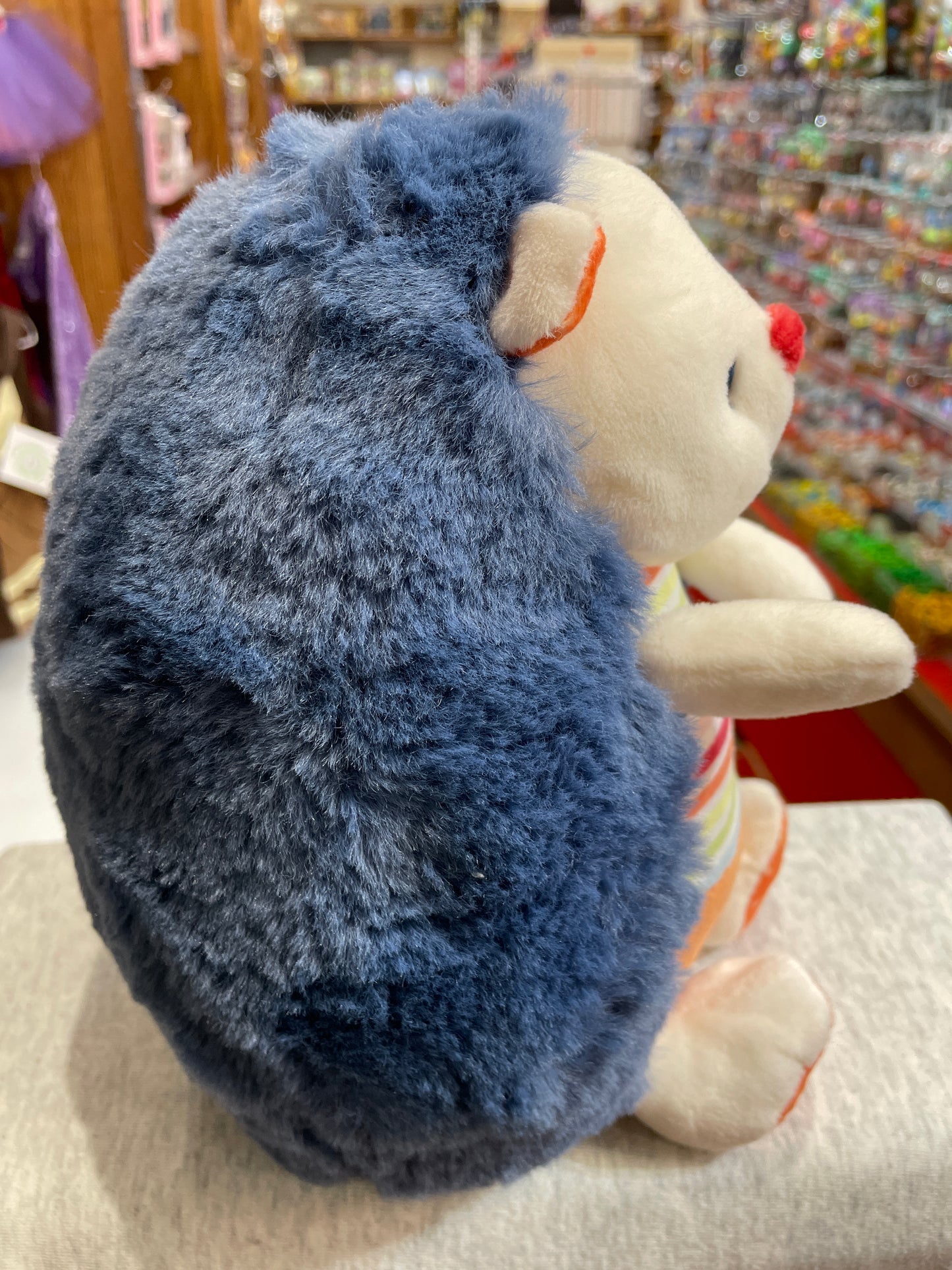 Gund Tinkle Crinkle hedgehog plush toy with navy blue fluffy back and colorful patterned body, sitting in toy store