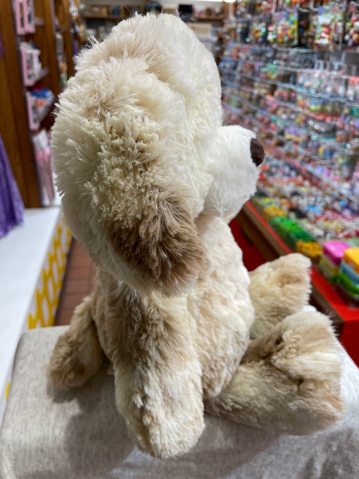 Fluffy white FabFuzz Arlo puppy plush toy sitting in toy store, soft fur and herringbone foot trim visible