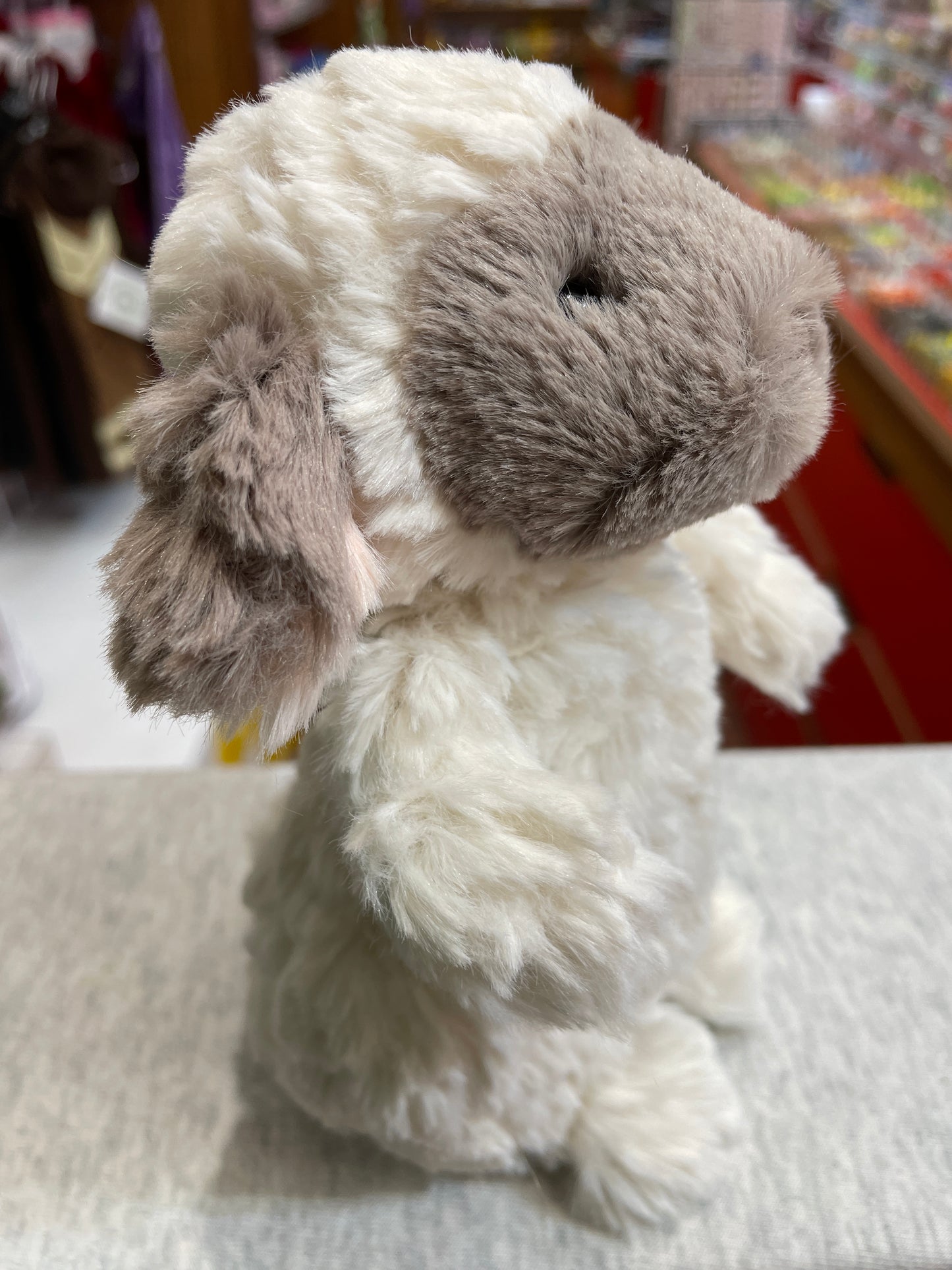 Soft Puttling lamb plush toy with white and gray fur, showcasing its fluffy texture and adorable profile in a store setting