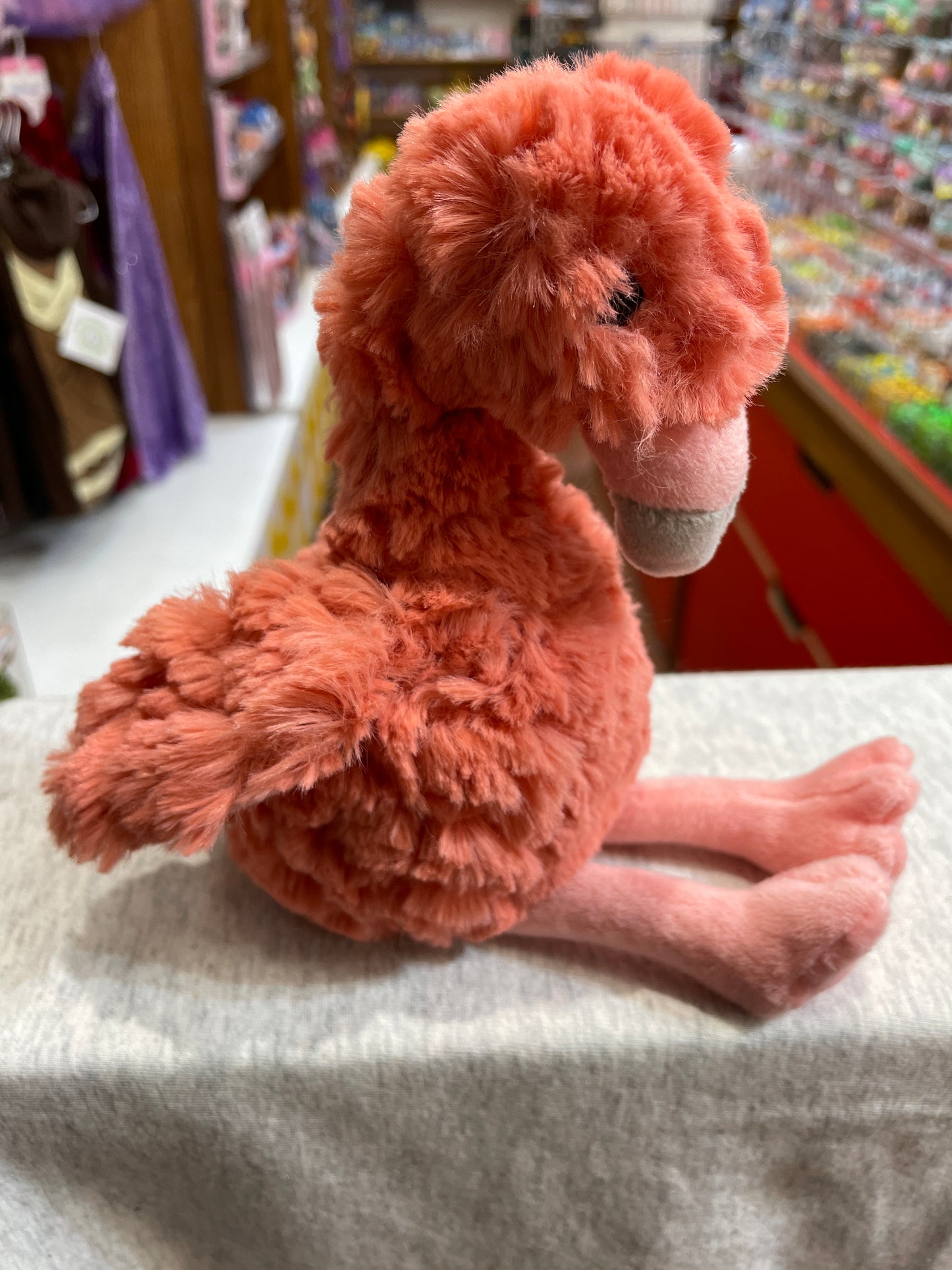 Soft, plush coral flamingo toy from Mary Meyer Puttling collection, sitting on display in store, with fluffy texture and sweet smile