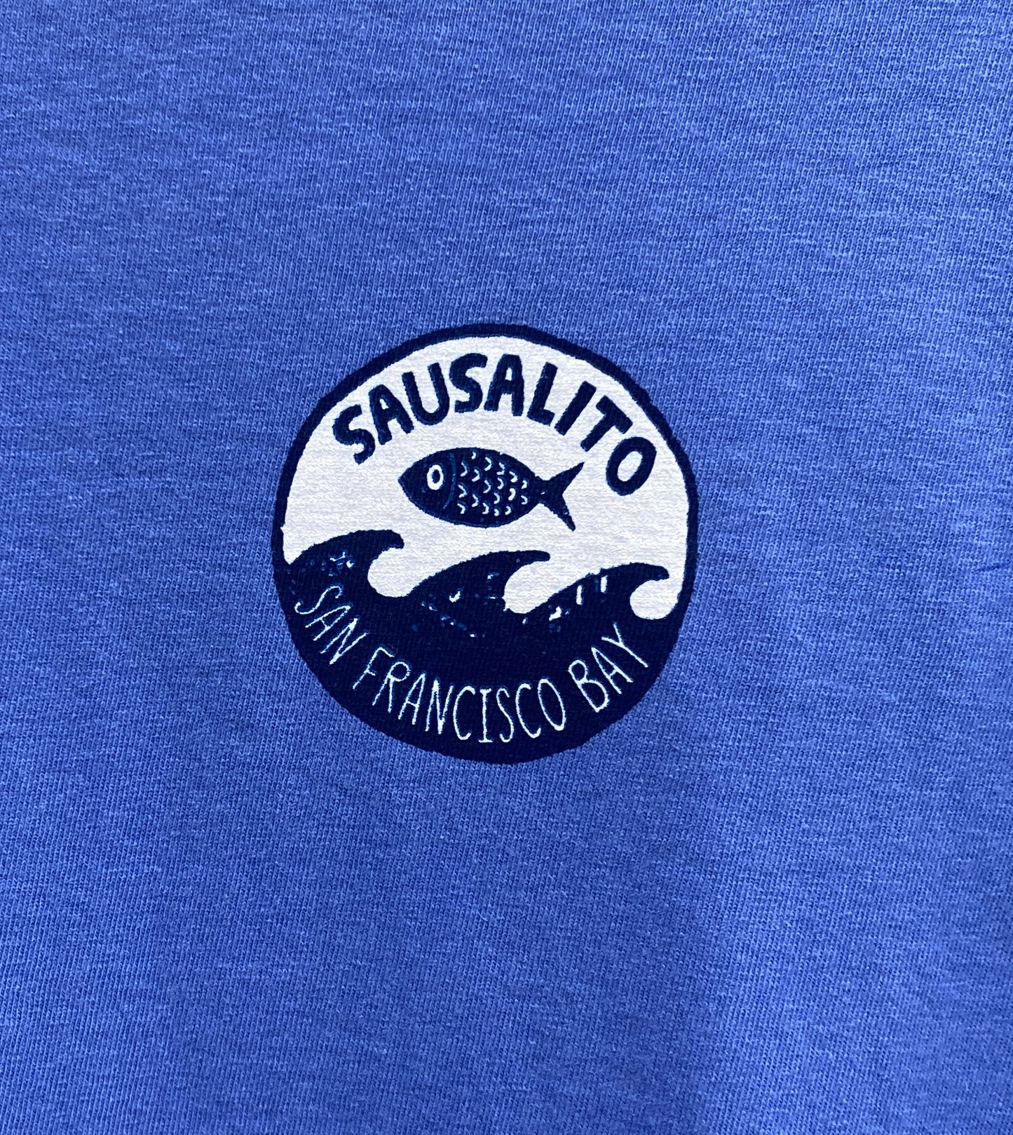 Sausalito Fish Wave logo on blue shirt, featuring San Francisco Bay waves and jumping fish design