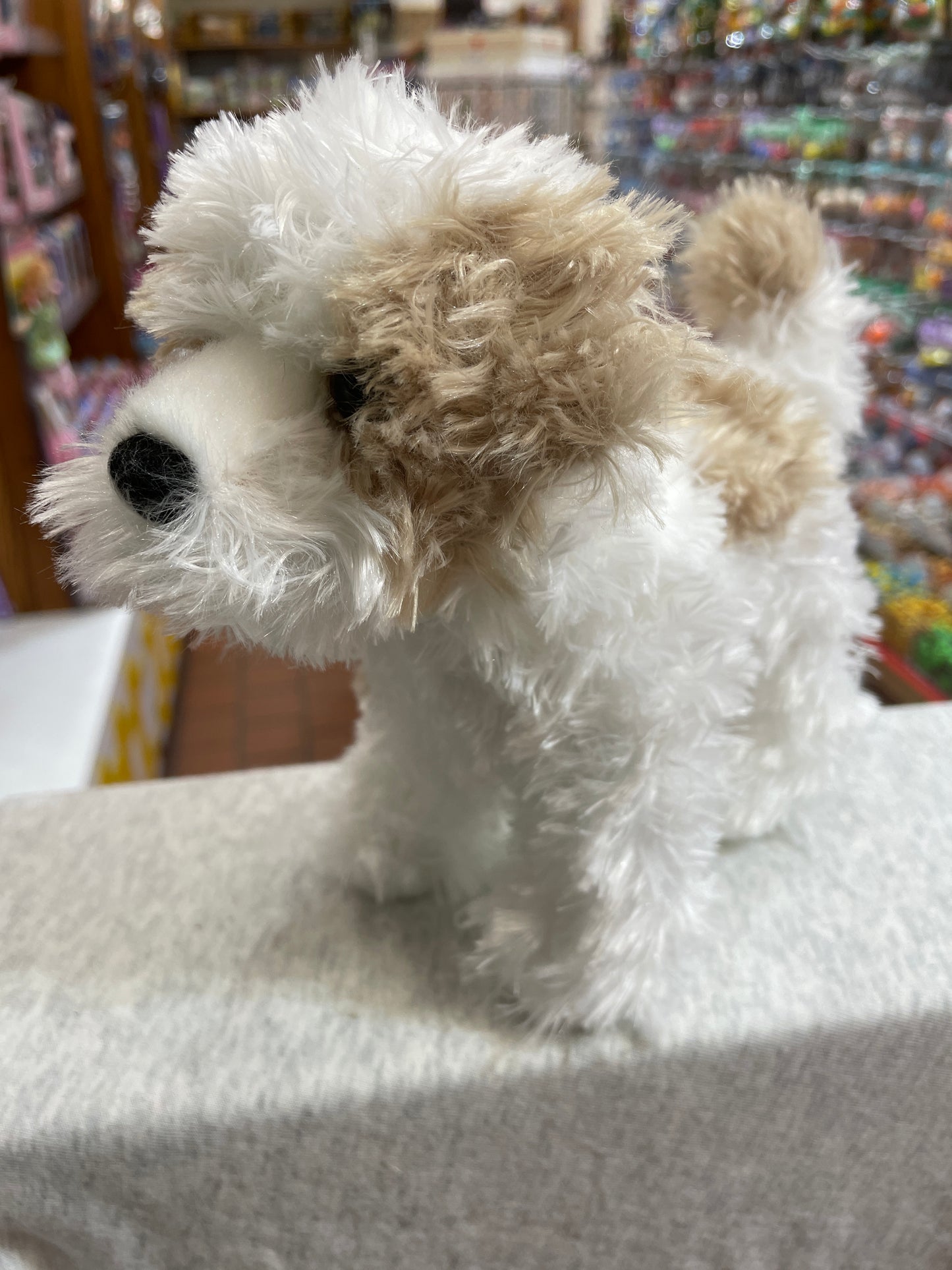 Adorable Maltipoo plush dog with fluffy white and tan fur, standing upright in a toy store display
