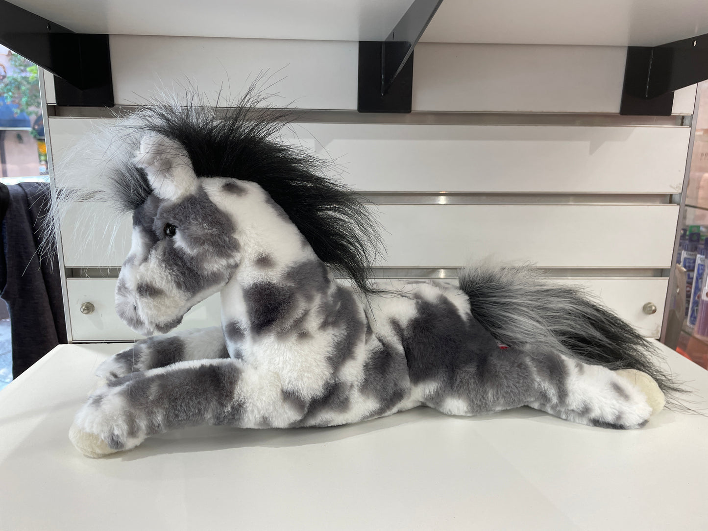 Plush Appaloosa horse toy with gray and white spotted coat, black mane and tail, lying down in floppy pose on display shelf