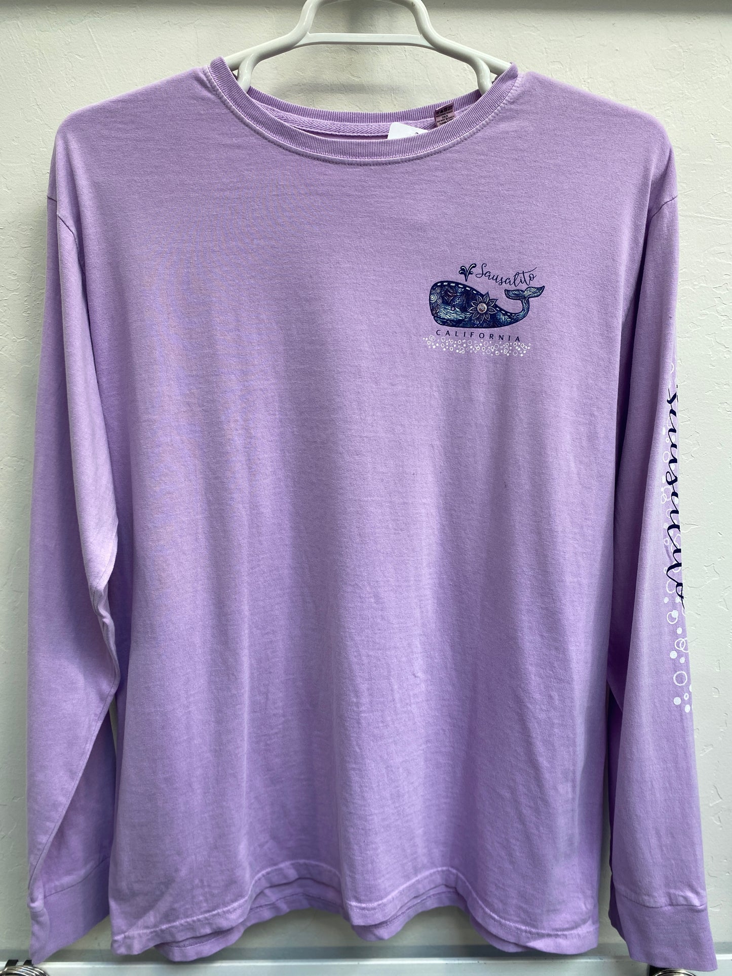 Lavender long sleeve t-shirt with decorative whale design and Sausalito California text, hanging on display