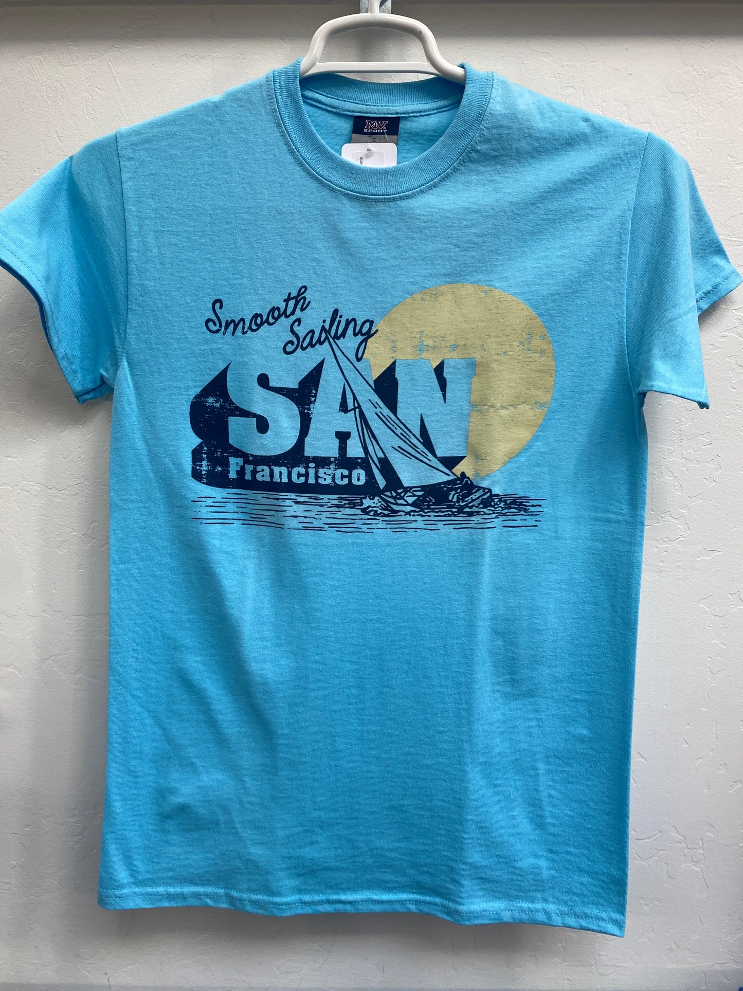 Blue t-shirt with "Smooth Sailing San Francisco" design featuring sailboat and sunset, hanging on display