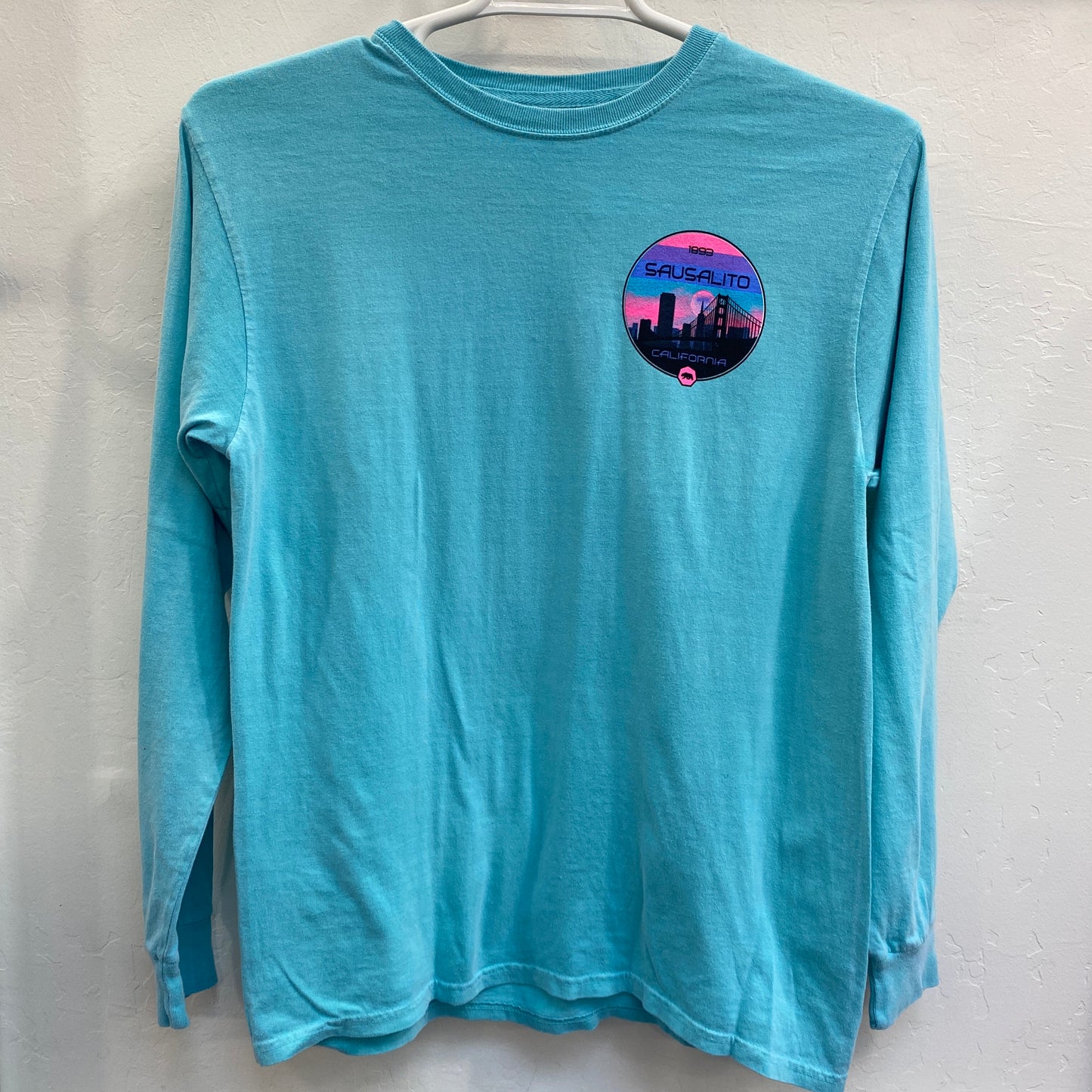 Teal long sleeve t-shirt with colorful Sausalito San Francisco skyline logo on chest, featuring Golden Gate Bridge silhouette