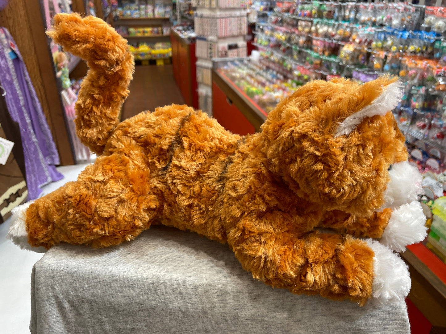 Soft, cuddly Gund orange tabby cat plush toy displayed in toy store, 14 inches long with poseable paws