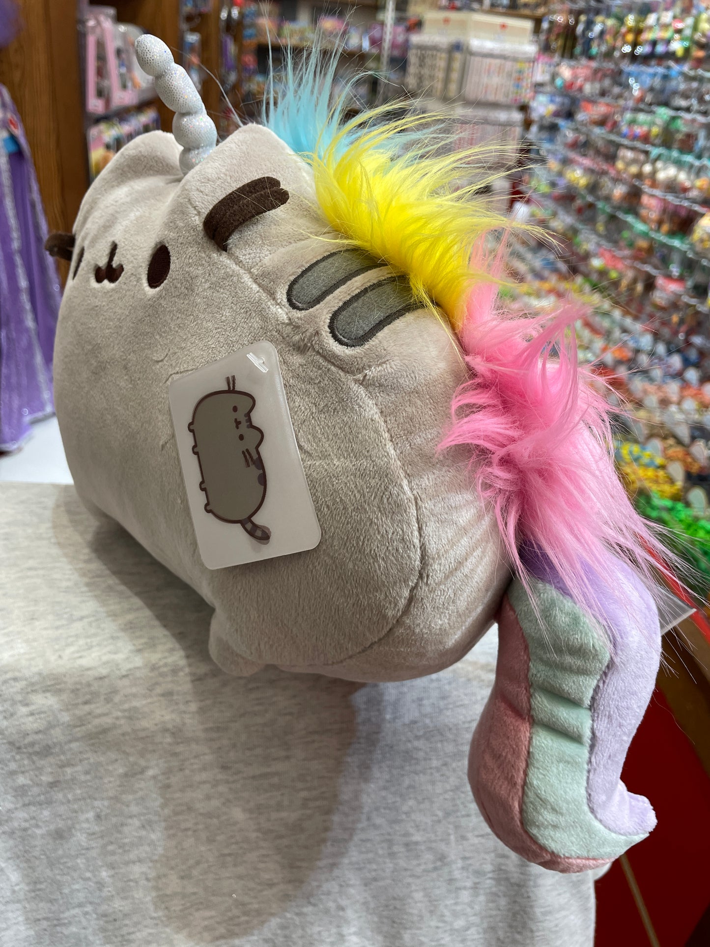 Gund Pusheen Pusheenicorn plush toy with rainbow mane, sparkly horn, and cat-shaped tag in toy store display