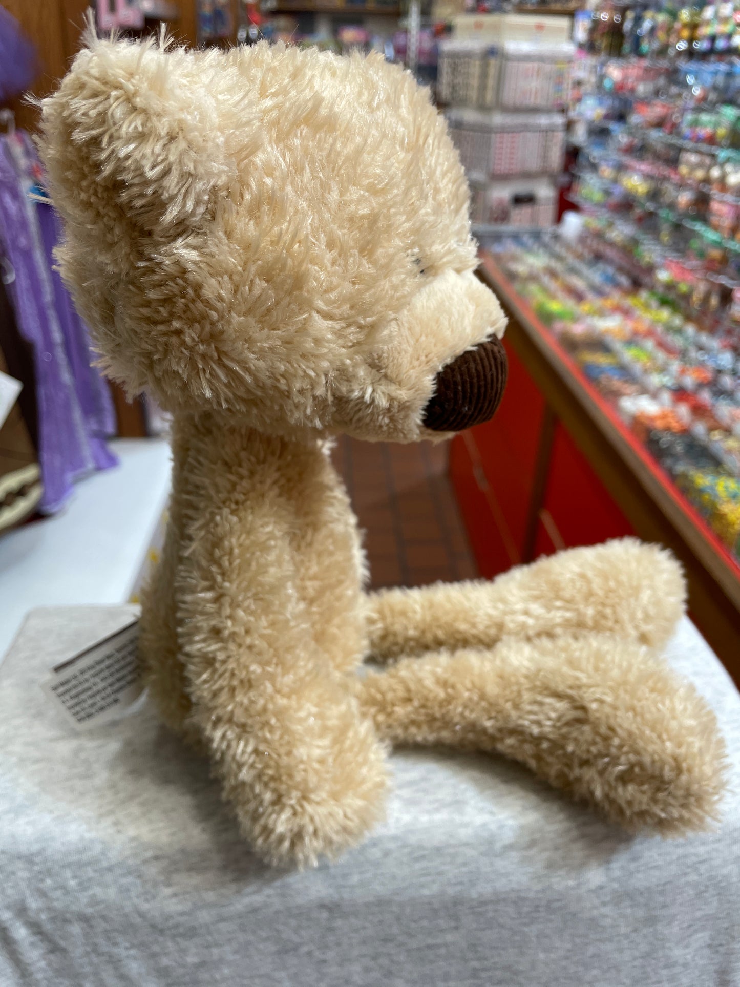 Gund Toothpick Bear plush toy, 15-inch soft beige teddy with slender body and modern design, sitting in toy store display