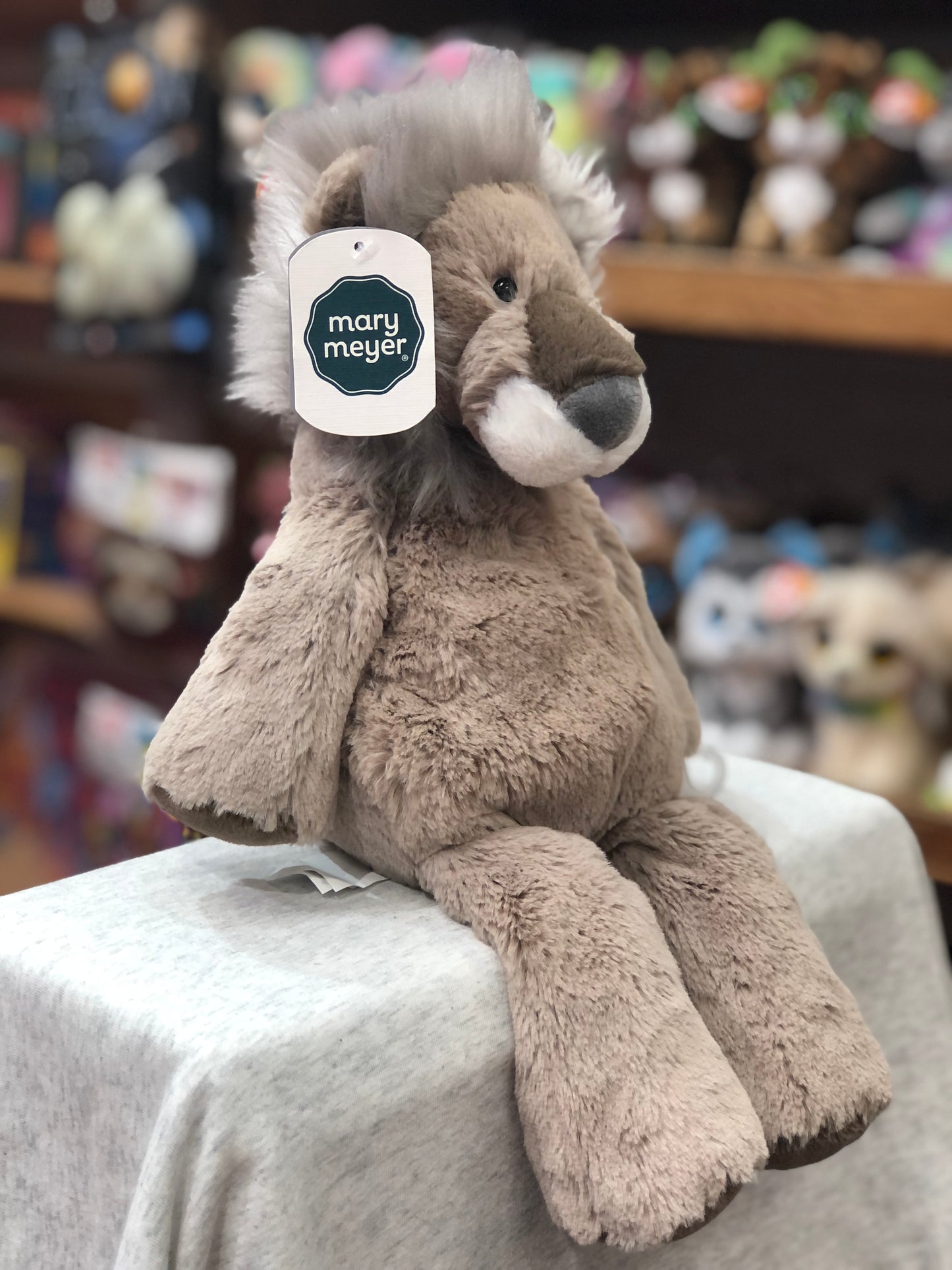Soft Mary Meyer Marshmallow Latte Lion plush toy, 13 inches, with fluffy mane and embroidered features, displayed in toy store