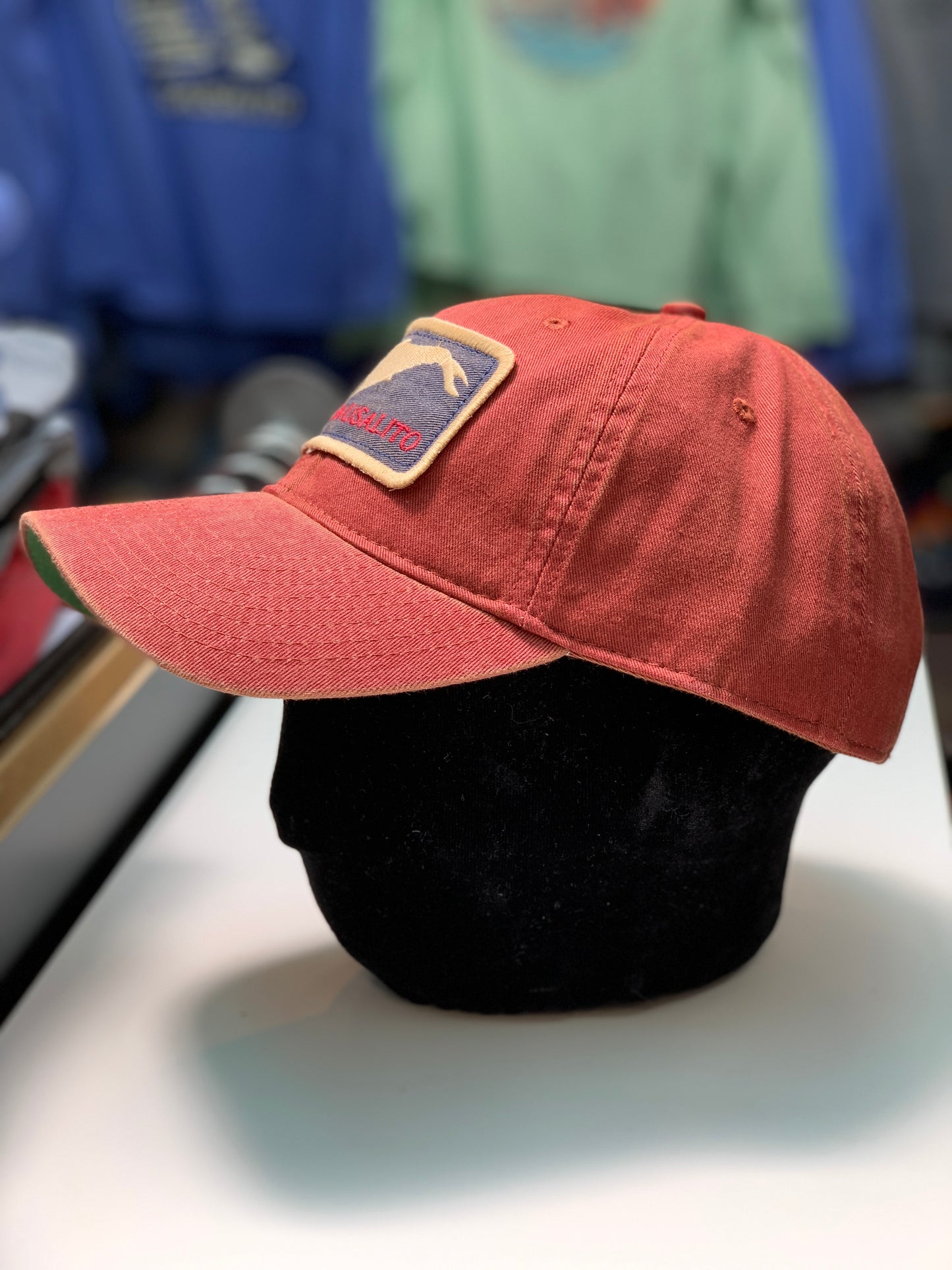 Red Sausalito California Grey Whale cotton cap with adjustable strap, displayed on stand in store