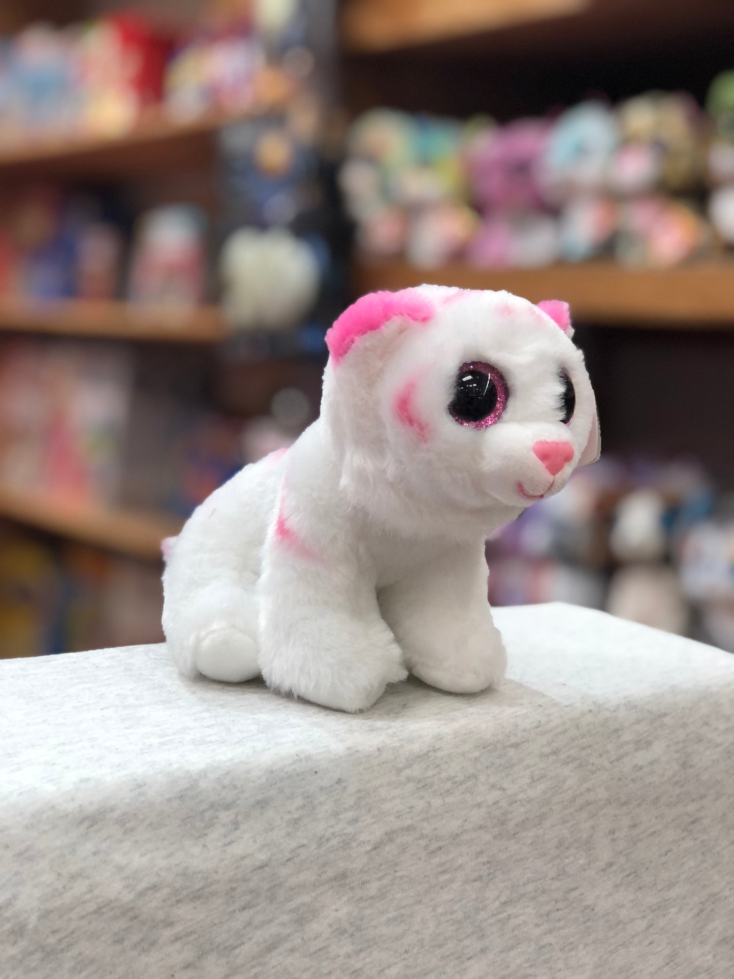 Ty Beanie Baby Tabor: White and pink tiger plush toy with bright eyes, sitting on display with other plush toys in background