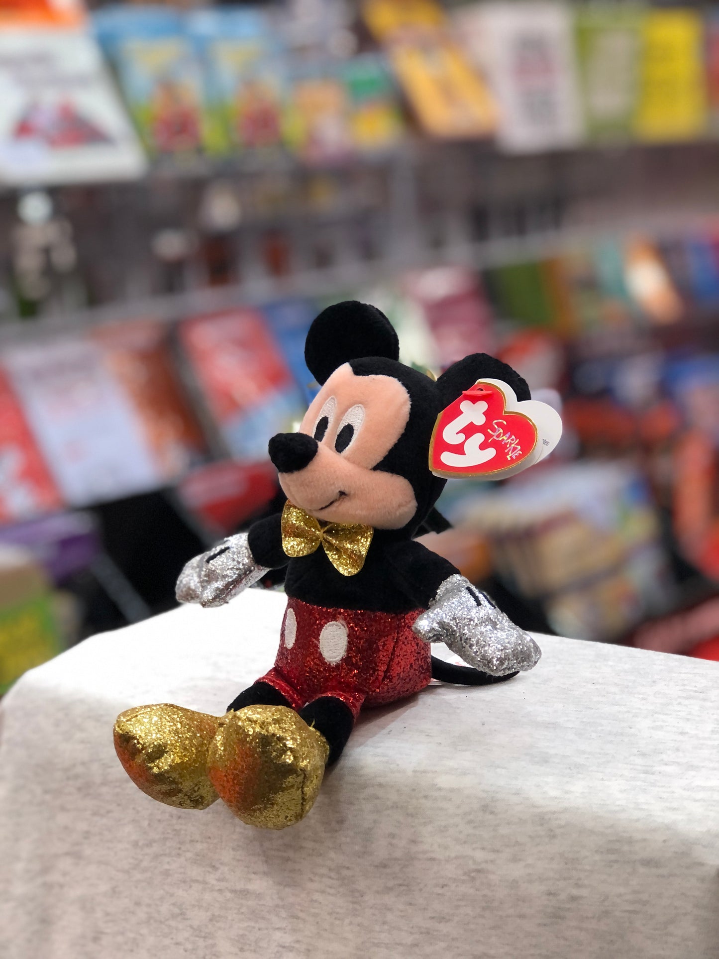 Ty Mickey Mouse plush with sparkly red shorts, gold bow tie, and silver gloves, displayed in toy store