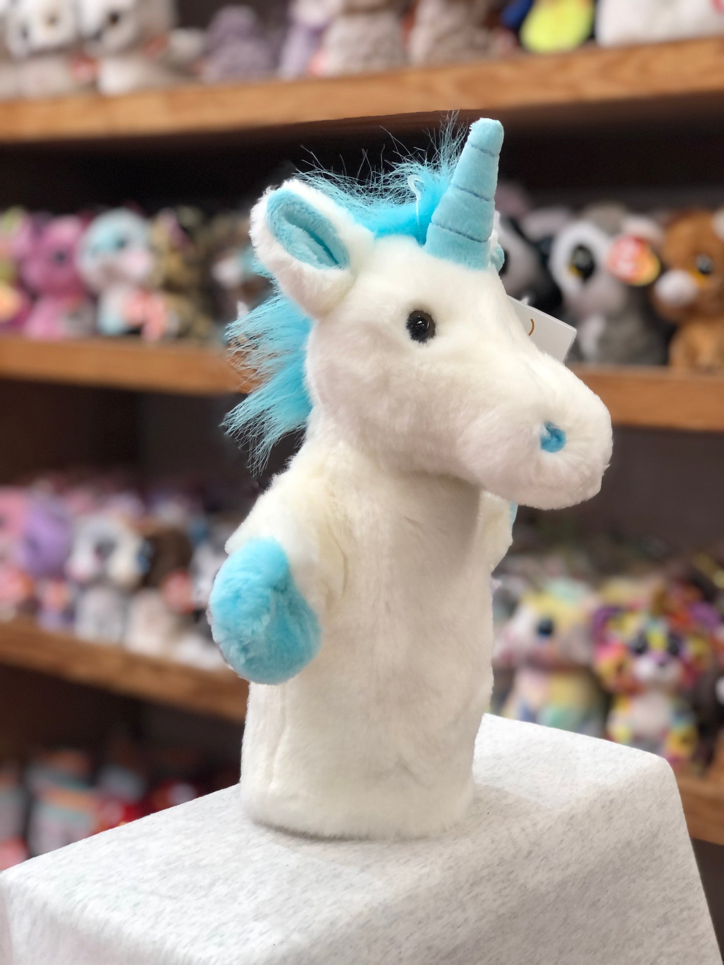Blue and white unicorn hand puppet from The Puppet Company's CarPets collection, displayed on shelf with other toys