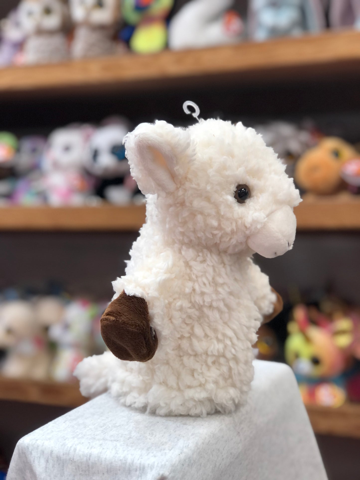 Fluffy white lamb hand puppet from CarPets collection, displayed on shelf with other toys, for family car entertainment