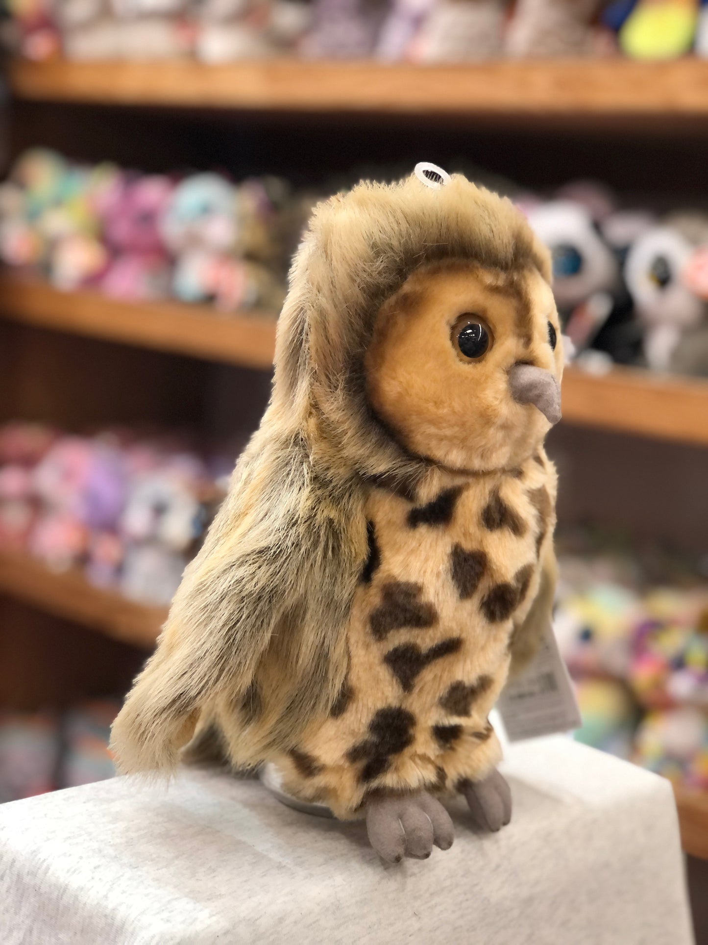 Cuddly full-bodied owl puppet with spotted chest, perched on display in toy store, showcasing realistic features and soft plush design