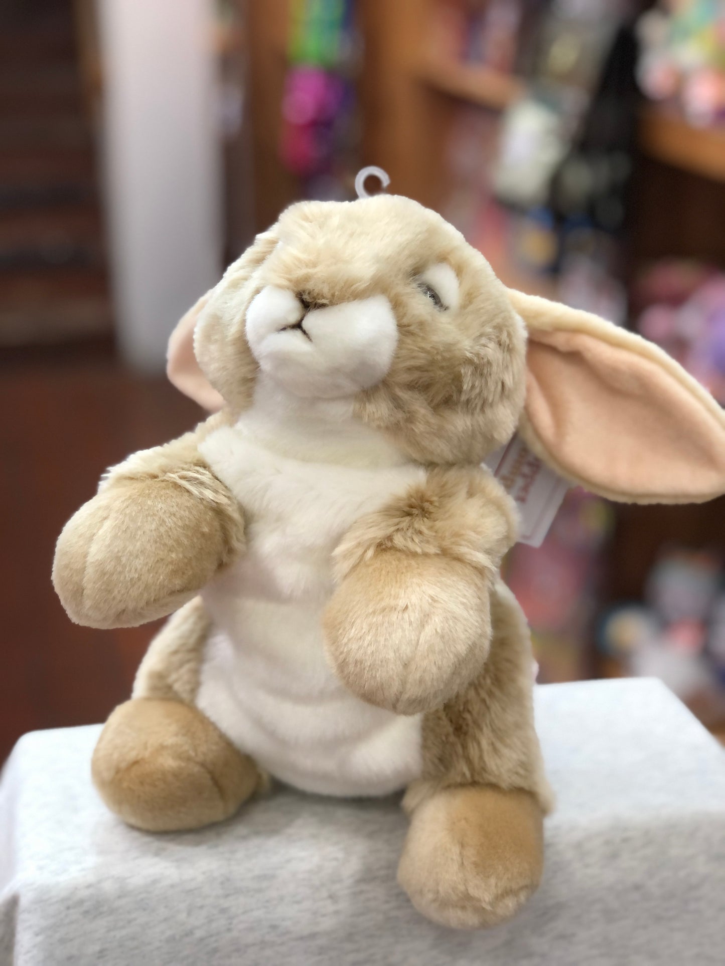Cuddly lop-eared rabbit puppet with soft beige fur, long floppy ears, and white belly, sitting on display in a toy store