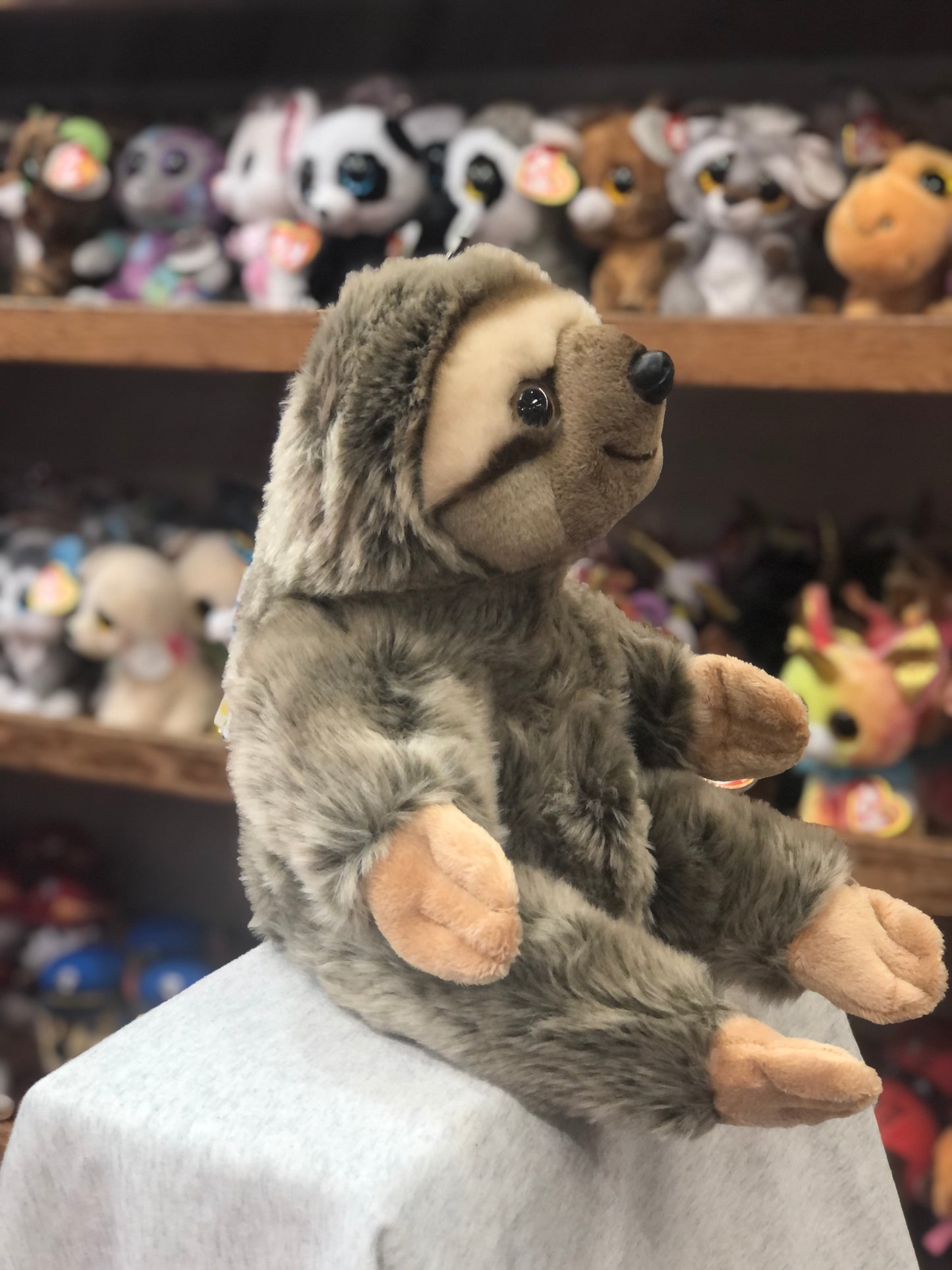 Cuddly full-bodied sloth puppet with soft gray fur, sitting on display with colorful animal toys in background