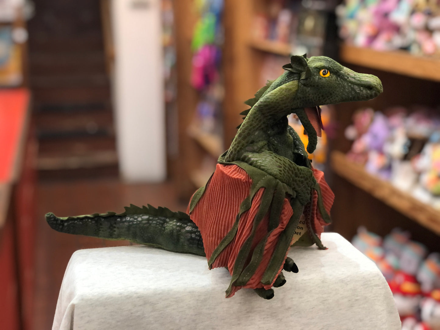 Folkmanis green dragon hand puppet with red wings, open mouth, sitting on display in toy store