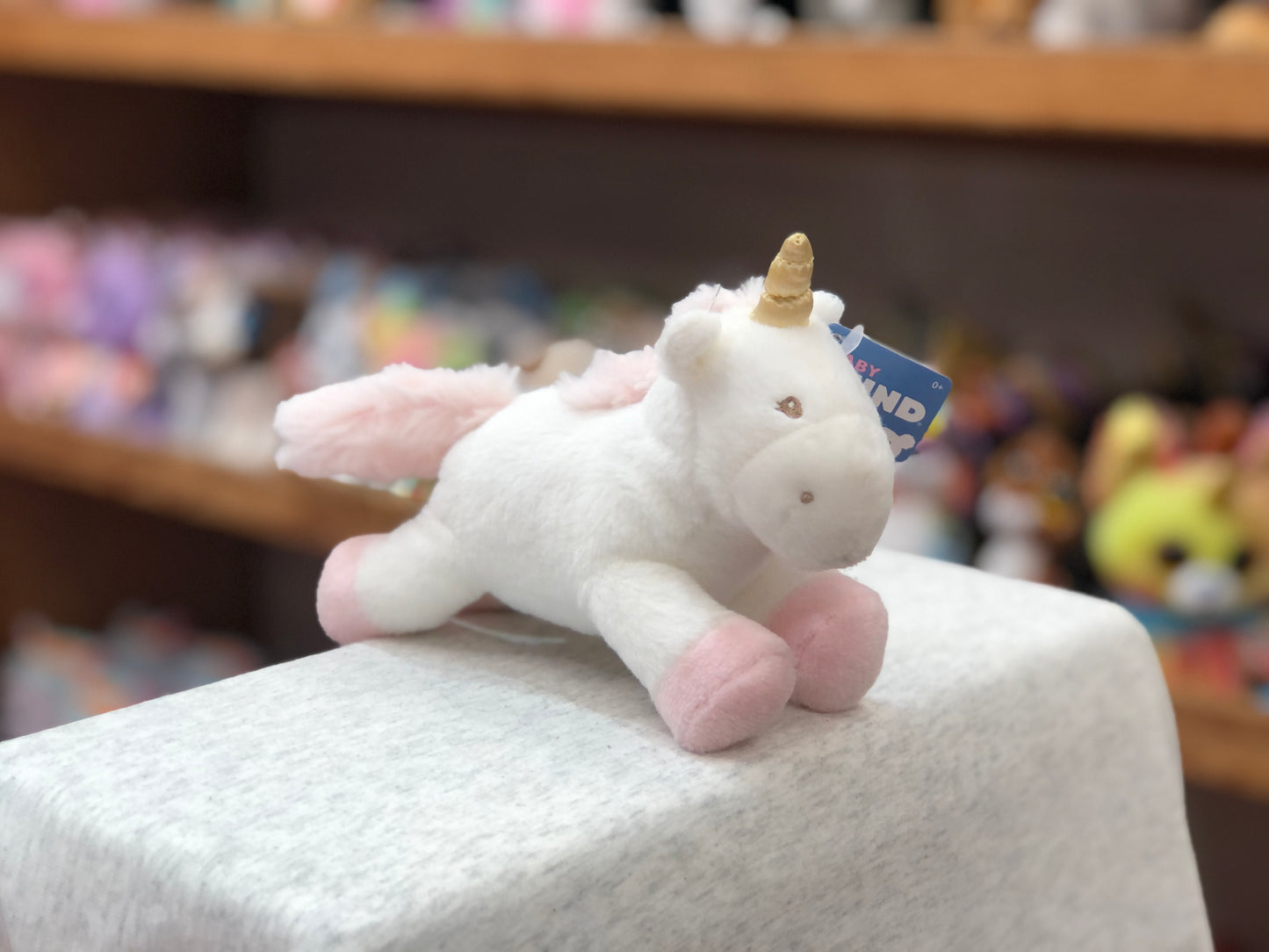 Gund Luna unicorn plush rattle toy with pink mane and golden horn, displayed on white surface in toy store