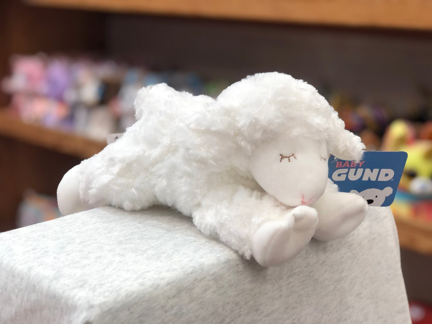 Soft white Gund Baby Winky Lamb rattle toy on display, featuring plush fur and closed eyes, with product tag visible