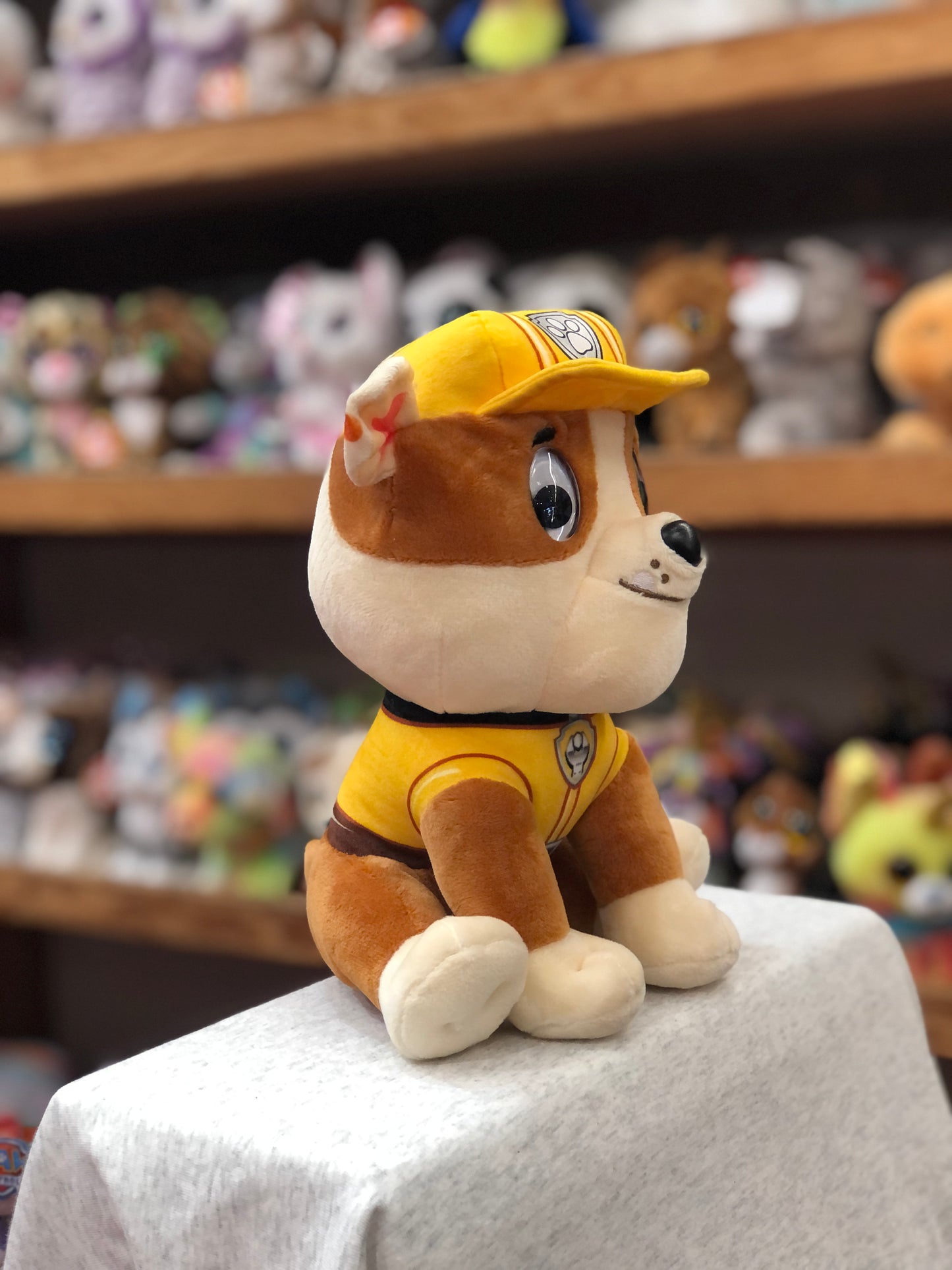 Gund Paw Patrol Rubble plush toy in yellow construction uniform, sitting on display with other stuffed animals in background
